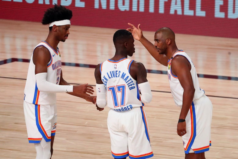Three Oklahoma City players stand together conversing on the basketball court.