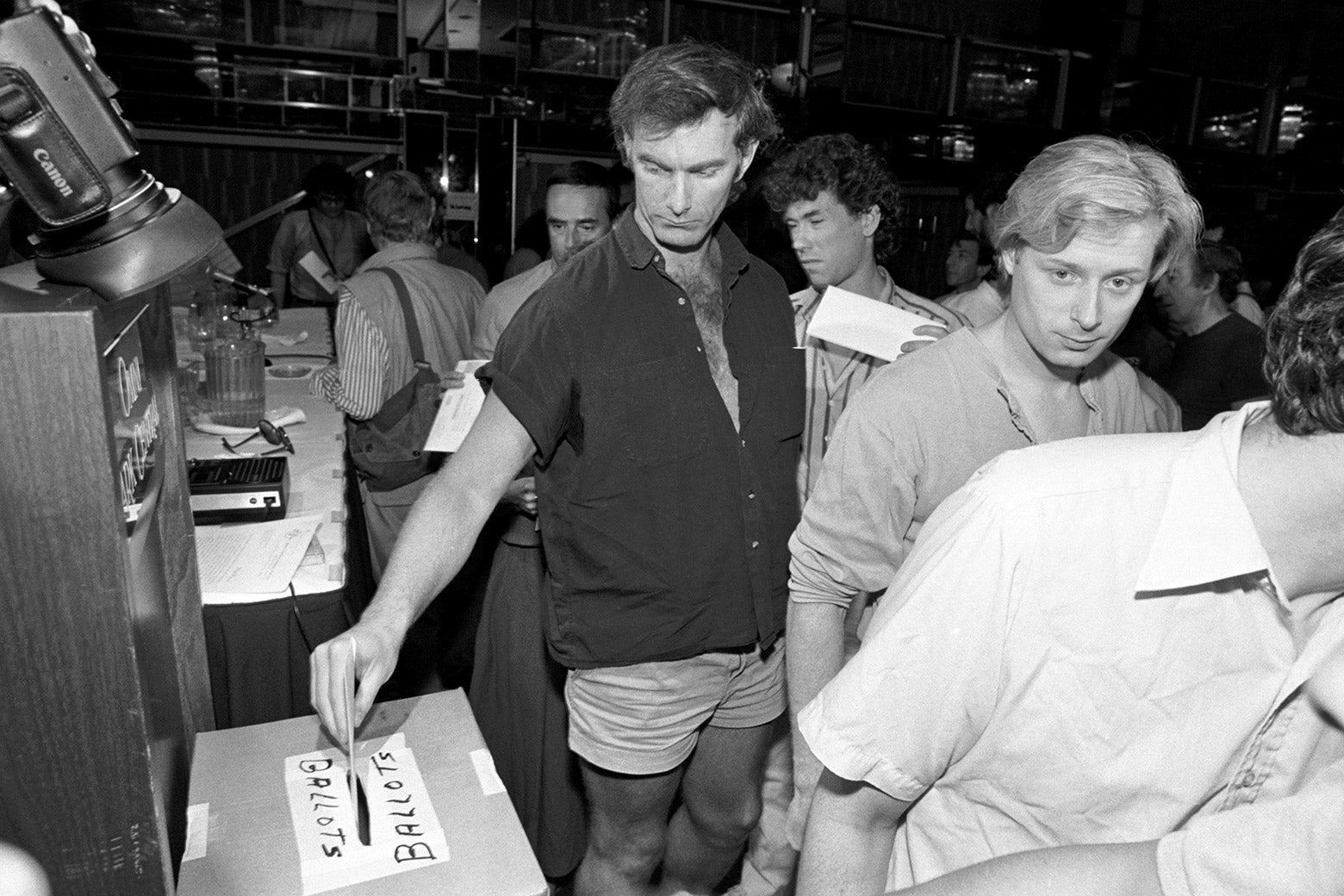 A black-and-white photo of John Sayles putting a ballot in a box.