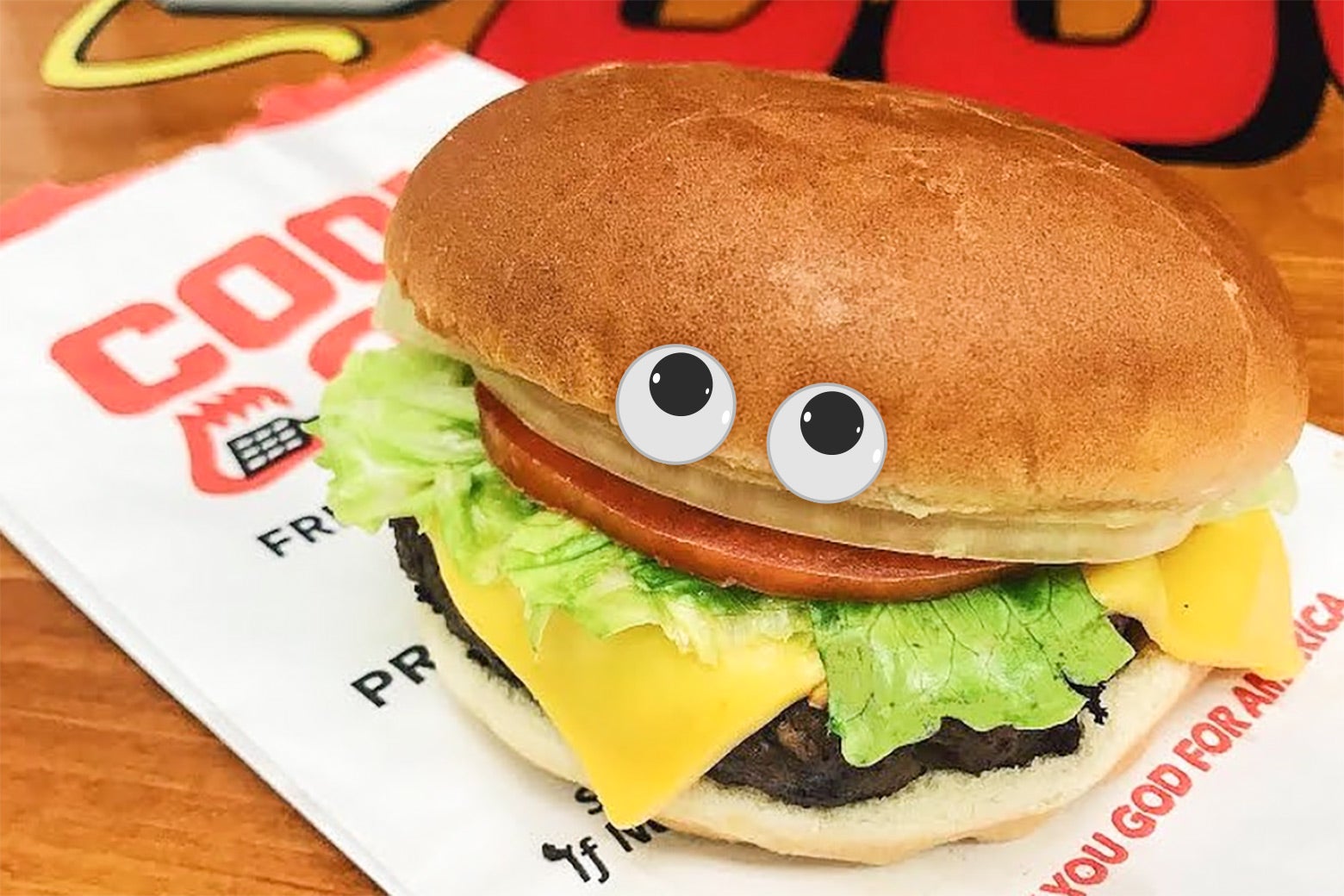 A fast-food cheeseburger, with googly eyes, sits expectantly atop a Cook Out bag.