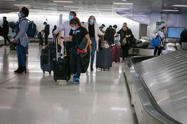Masked travelers retrieve their luggage from baggage claim