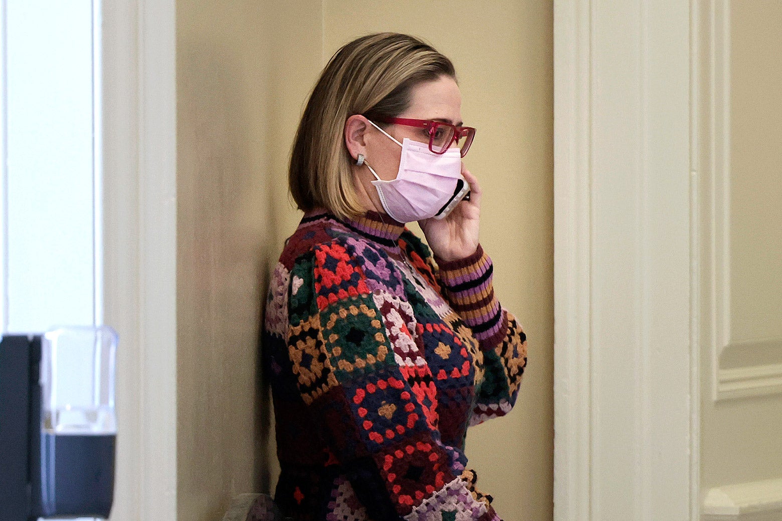Kyrsten Sinema, in a pink face mask, talks on a cell phone.