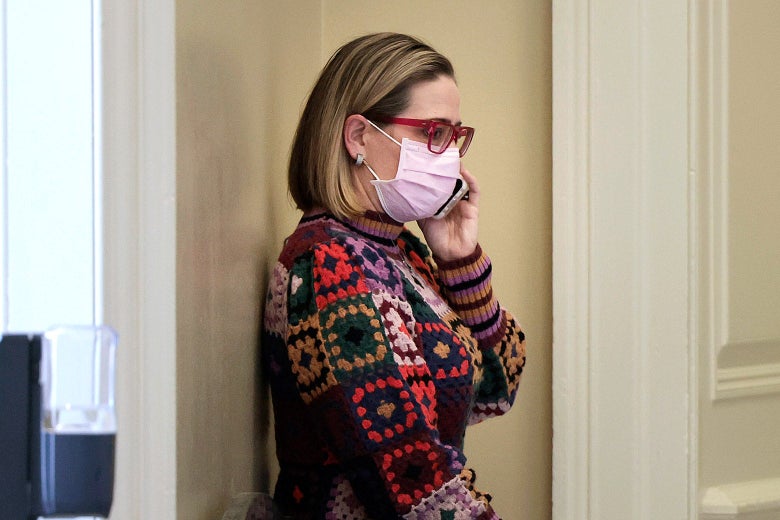 Kyrsten Sinema, in a pink face mask, talks on a cell phone.