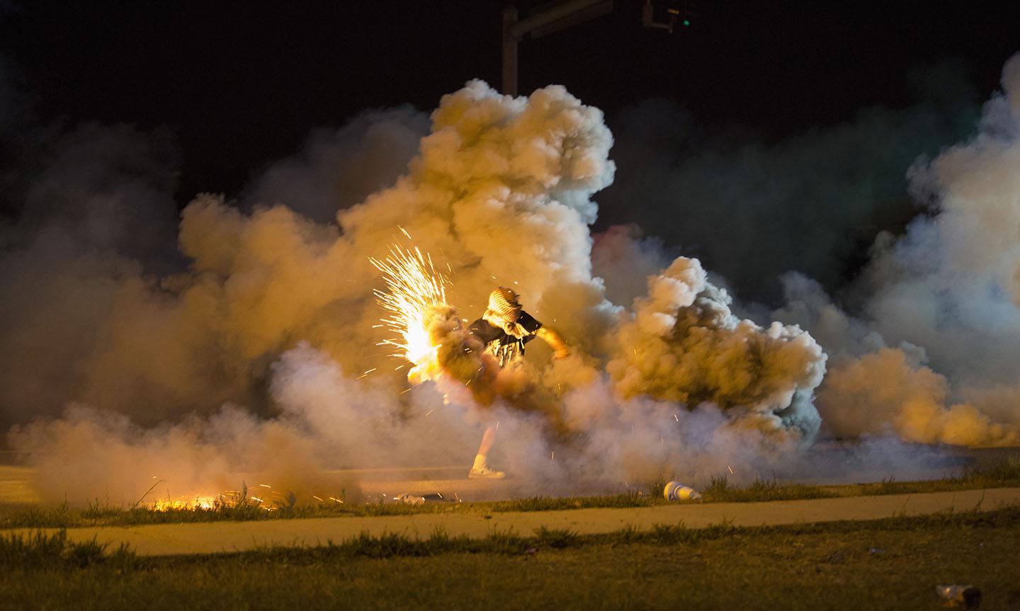 A protester throws back a smoke bomb while clashing with police in Ferguson, Missouri August 13, 2014.