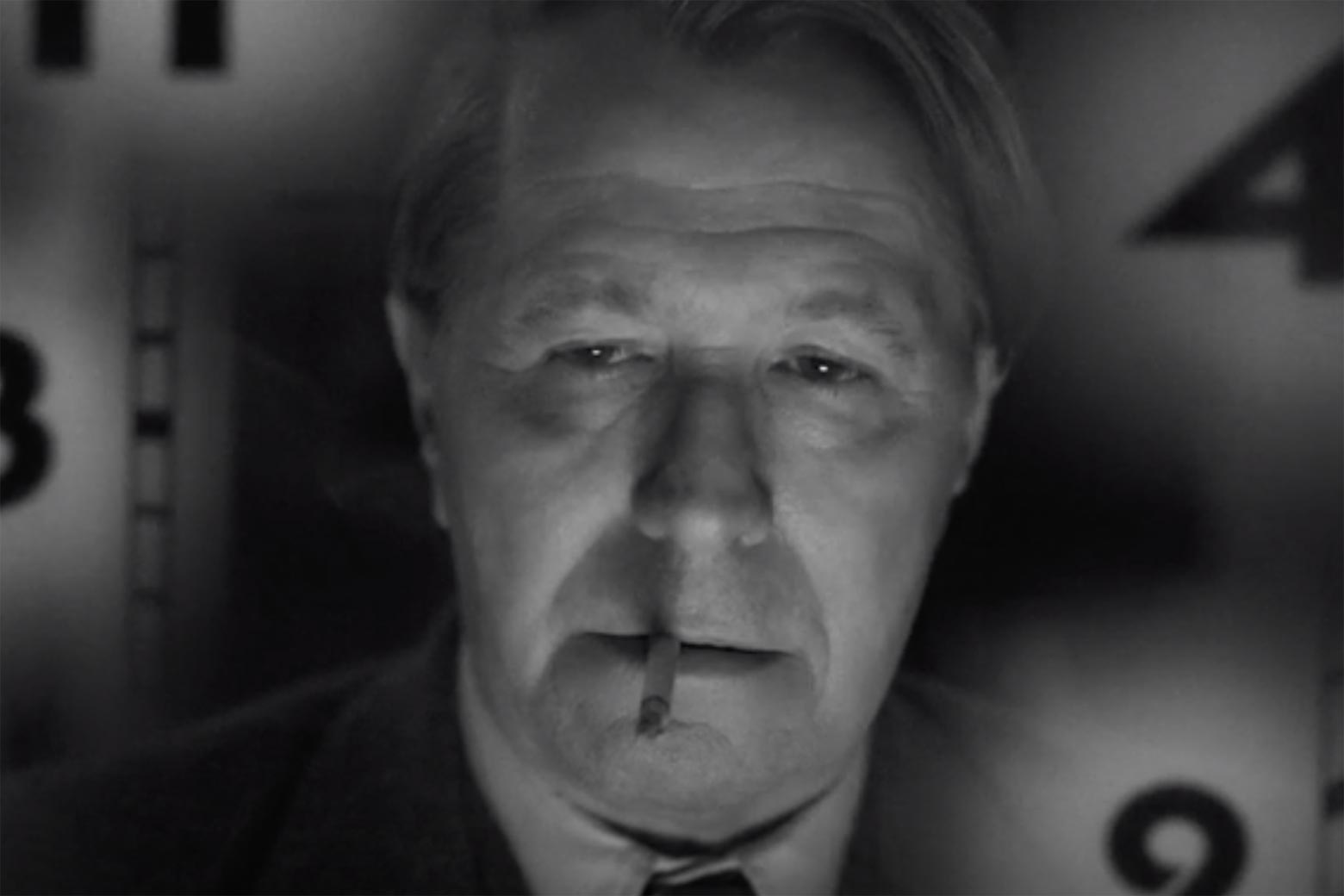 Black-and-white still of Gary Oldman with a cigarette in his mouth and numbers behind him.