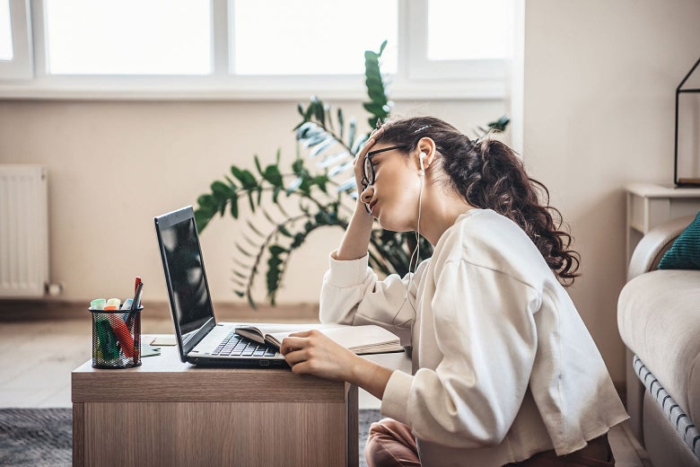 A woman in front of a laptop sits with her elbow on the desk, her hand propping up her head.