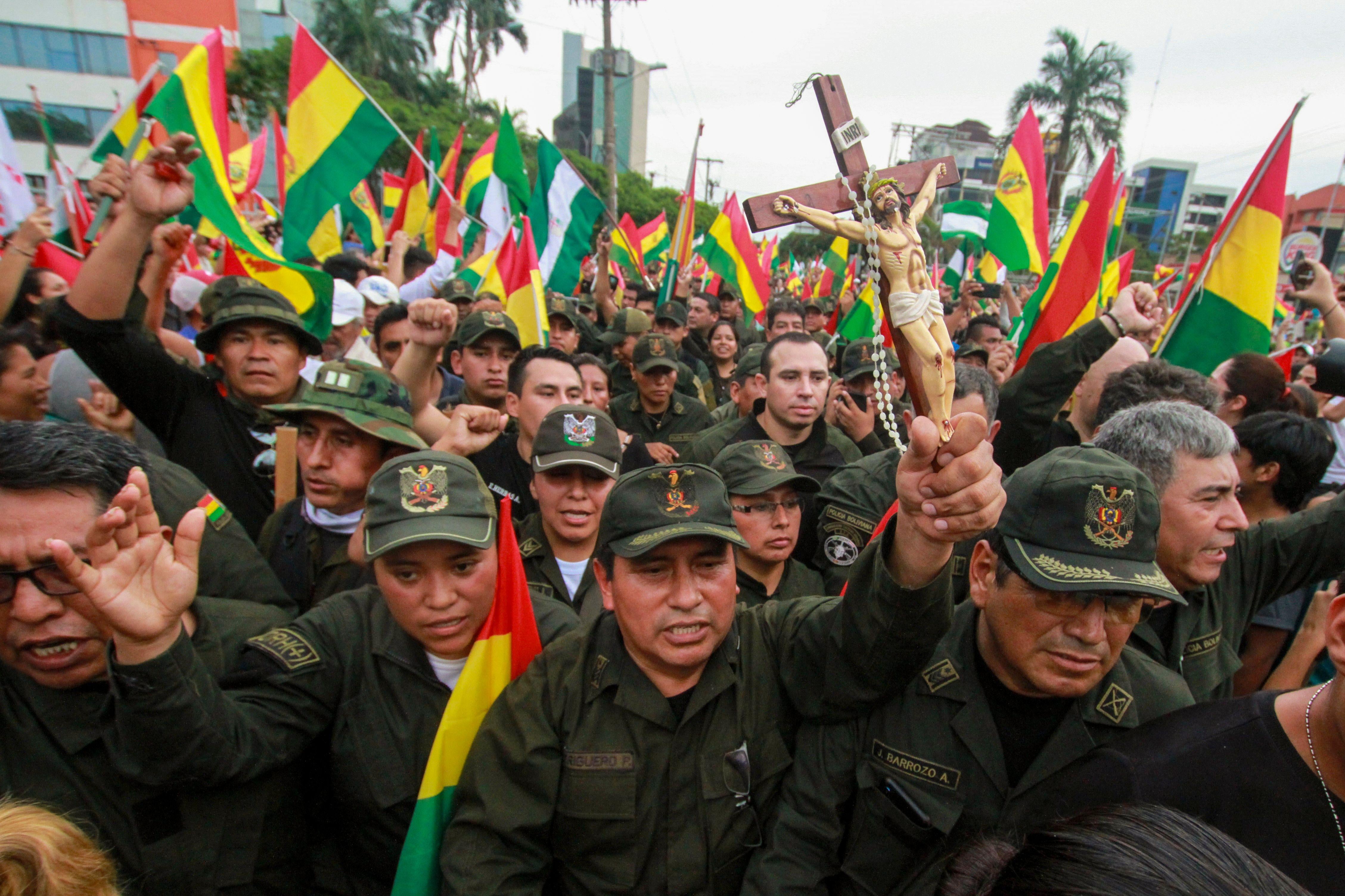 A police officer holds a crucifix among comrades and people taking to the streets of Santa Cruz to celebrate the resignation of Bolivian President Evo Morales on November 10, 2019.