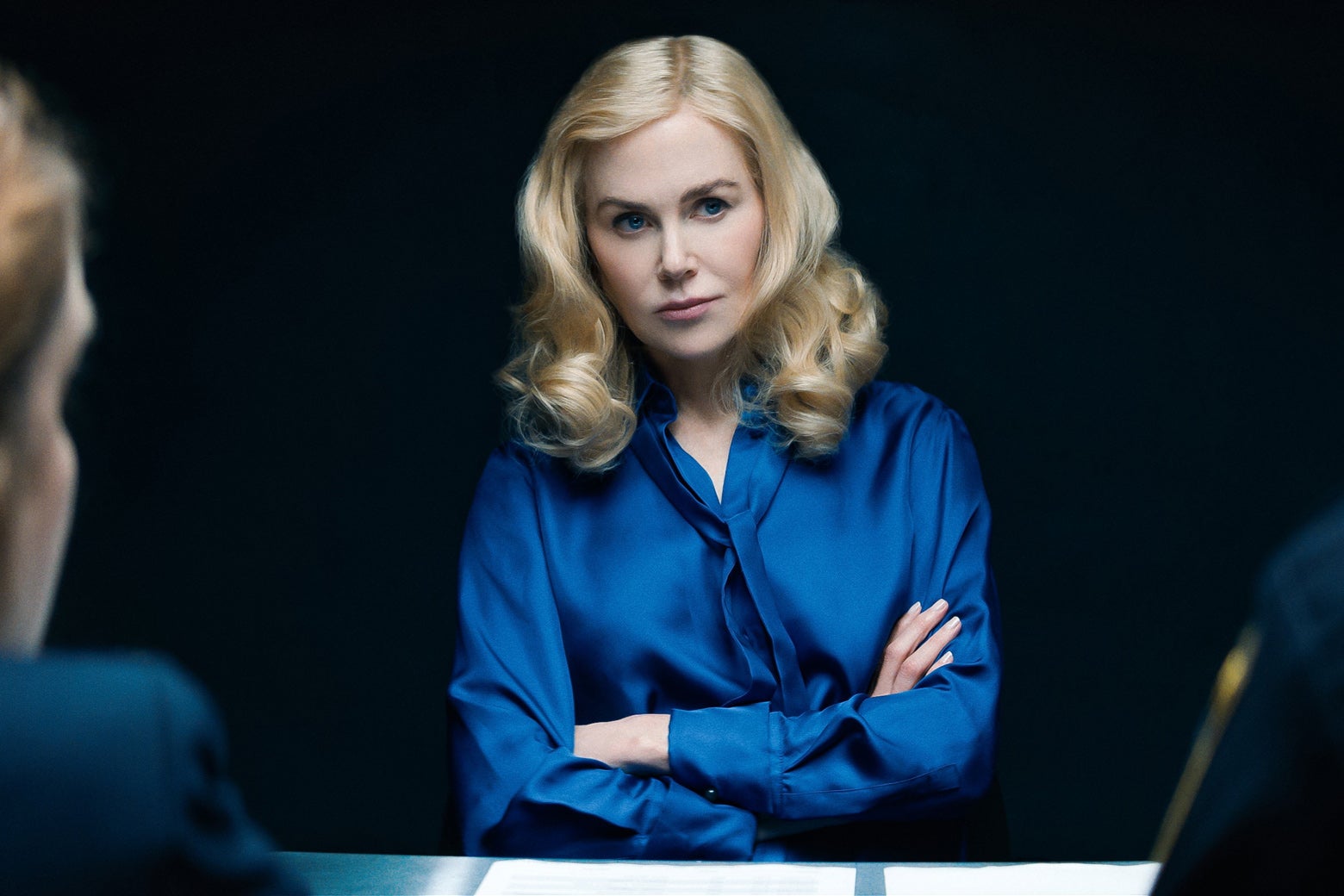 Nicole Kidman as Greer in the Perfect Couple, sitting with her arms folded in an interrogation room.