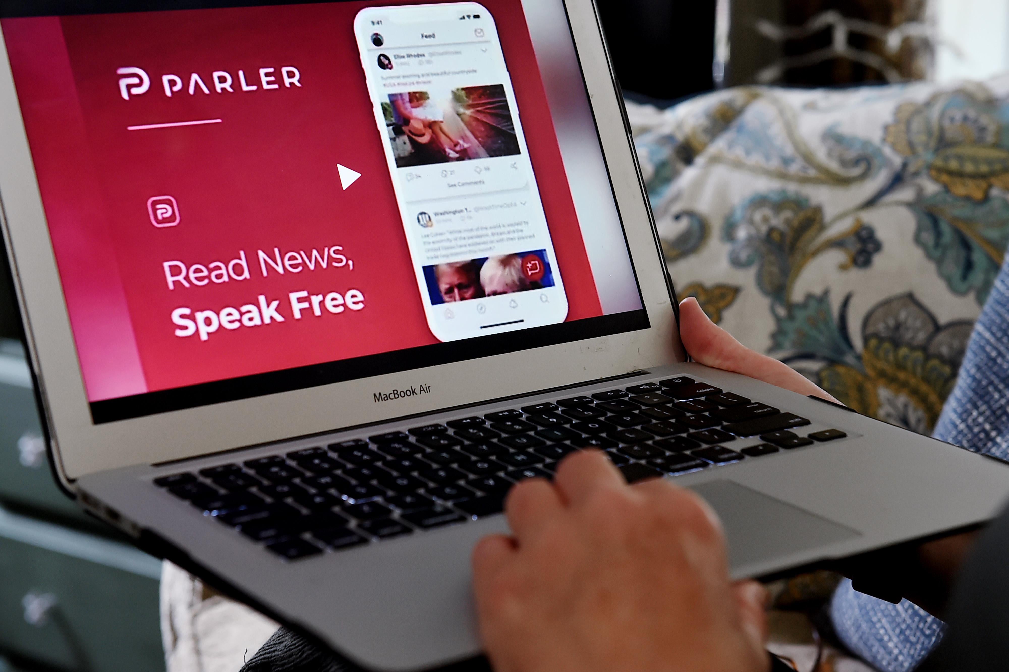 Hands hold a laptop that shows the homepage of Parler, which says, "Real News, Speak Free."