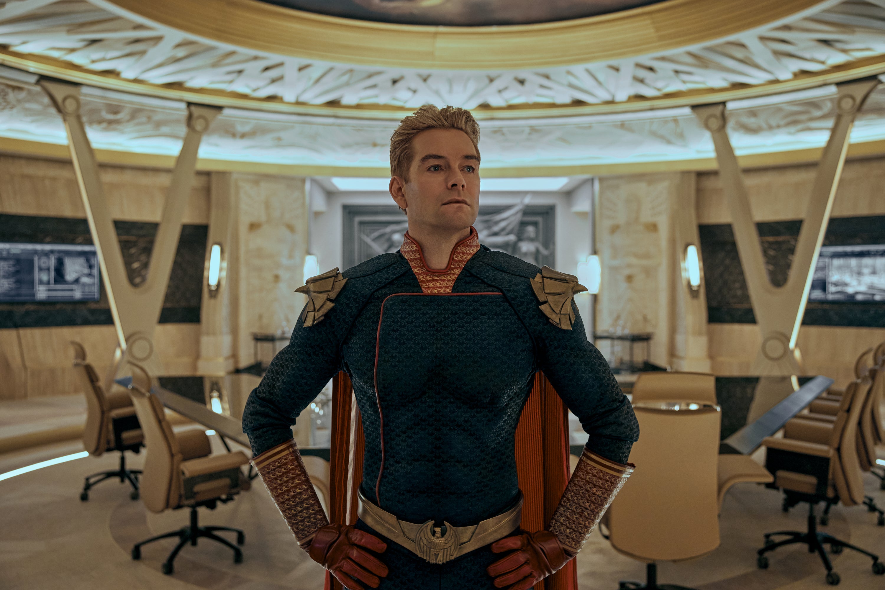 A superhero in a red white and blue costume stands in an ornate conference room, hands on his hips.