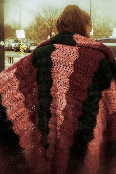 A woman wears a light blanket outside on a street. This image appears in the book EXPOSURE: Homelessness through the lens of art & poetry.