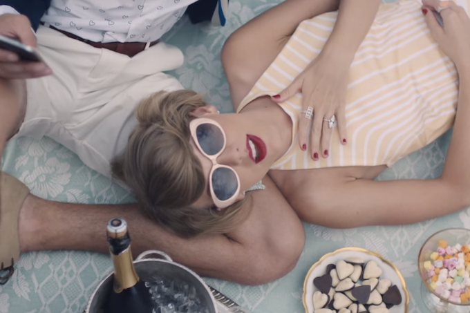 Taylor Swift lies back on a picnic blanket in sunglasses staring up at the viewer