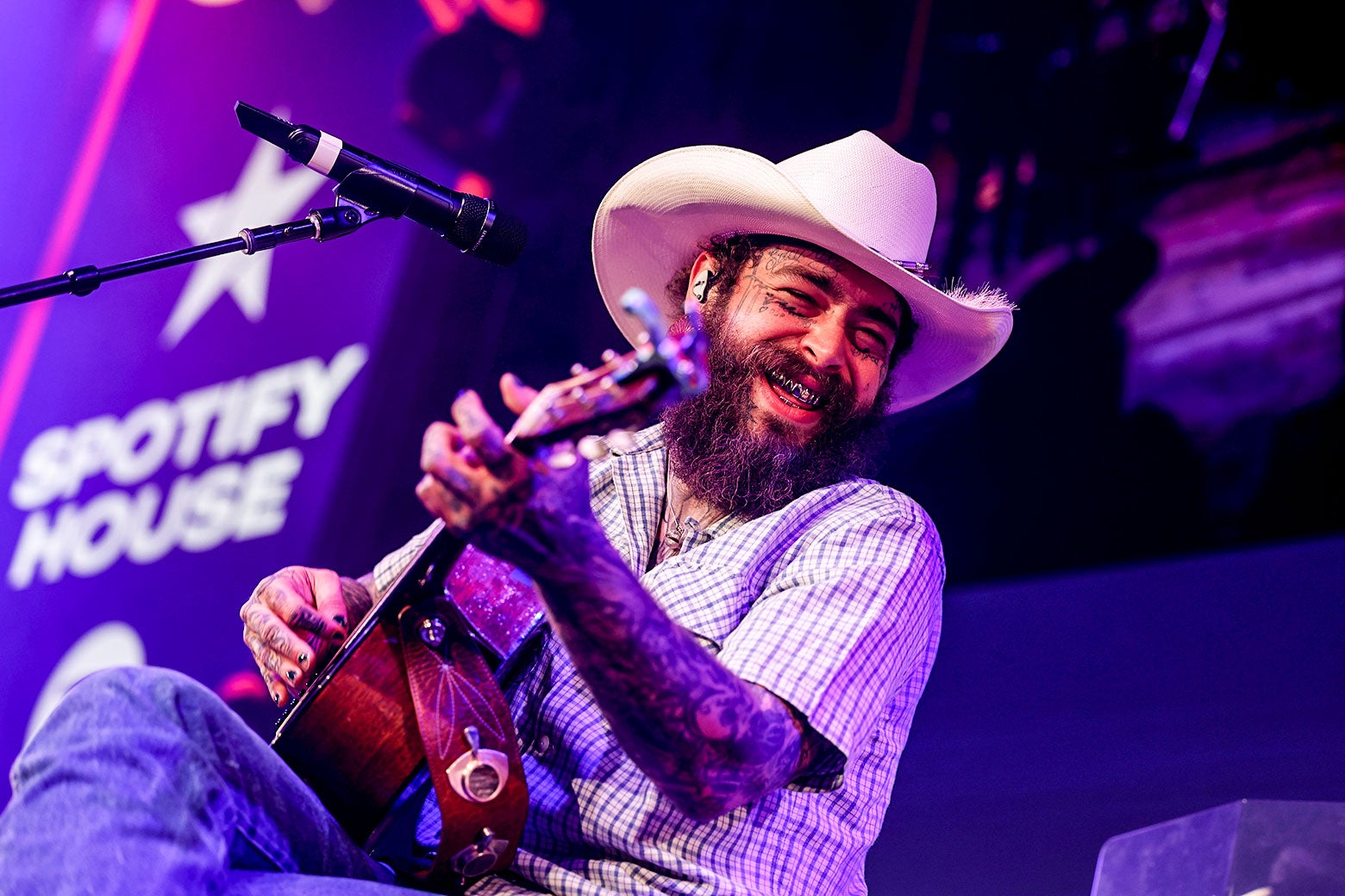 Post Malone leans back and smiles while playing guitar on stage.