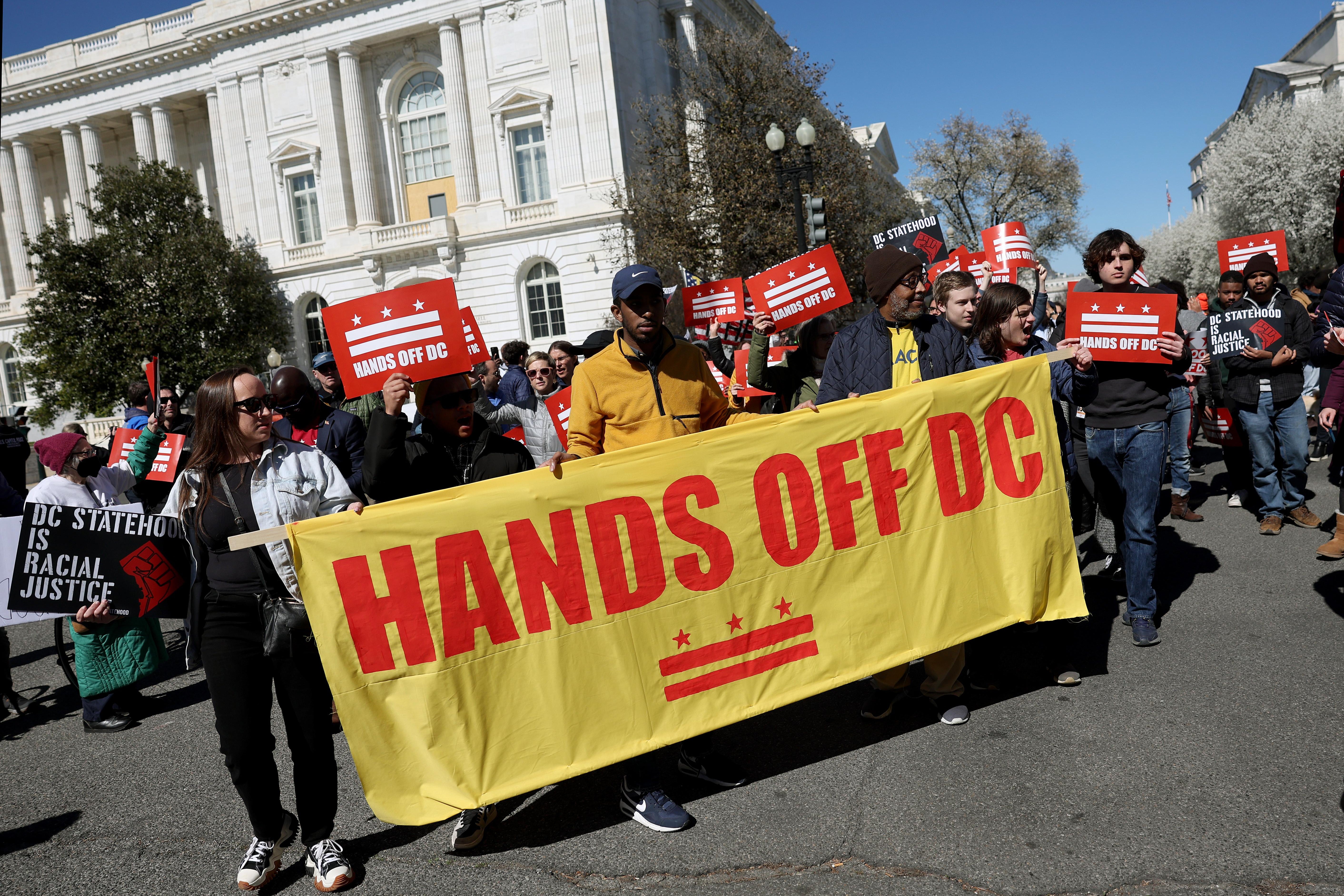 Demonstrators march in Washington, D.C., carrying a sign that says "Hands Off DC."