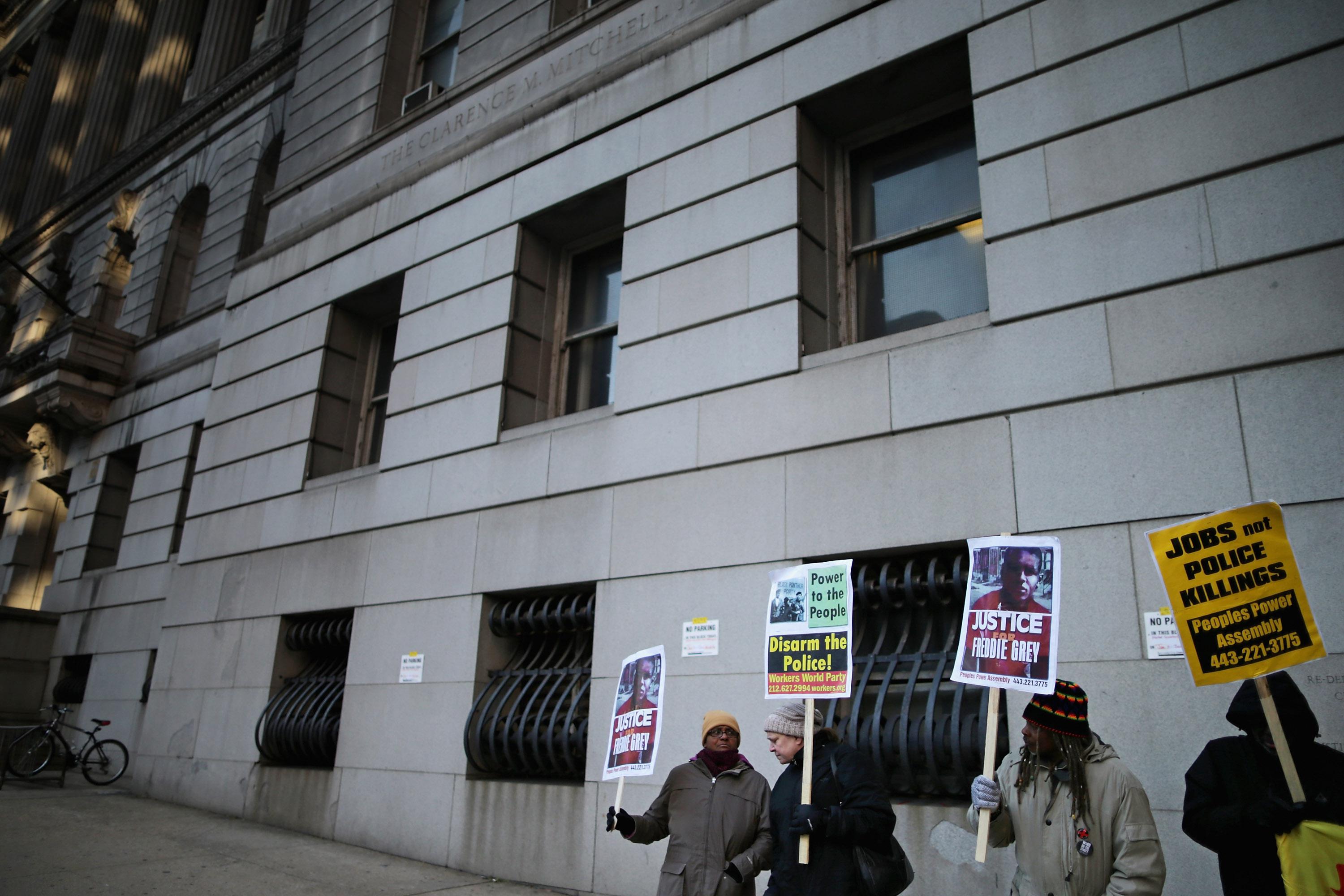 A group of protesters outside a courthouse hold signs demanding justice for Freddie Gray