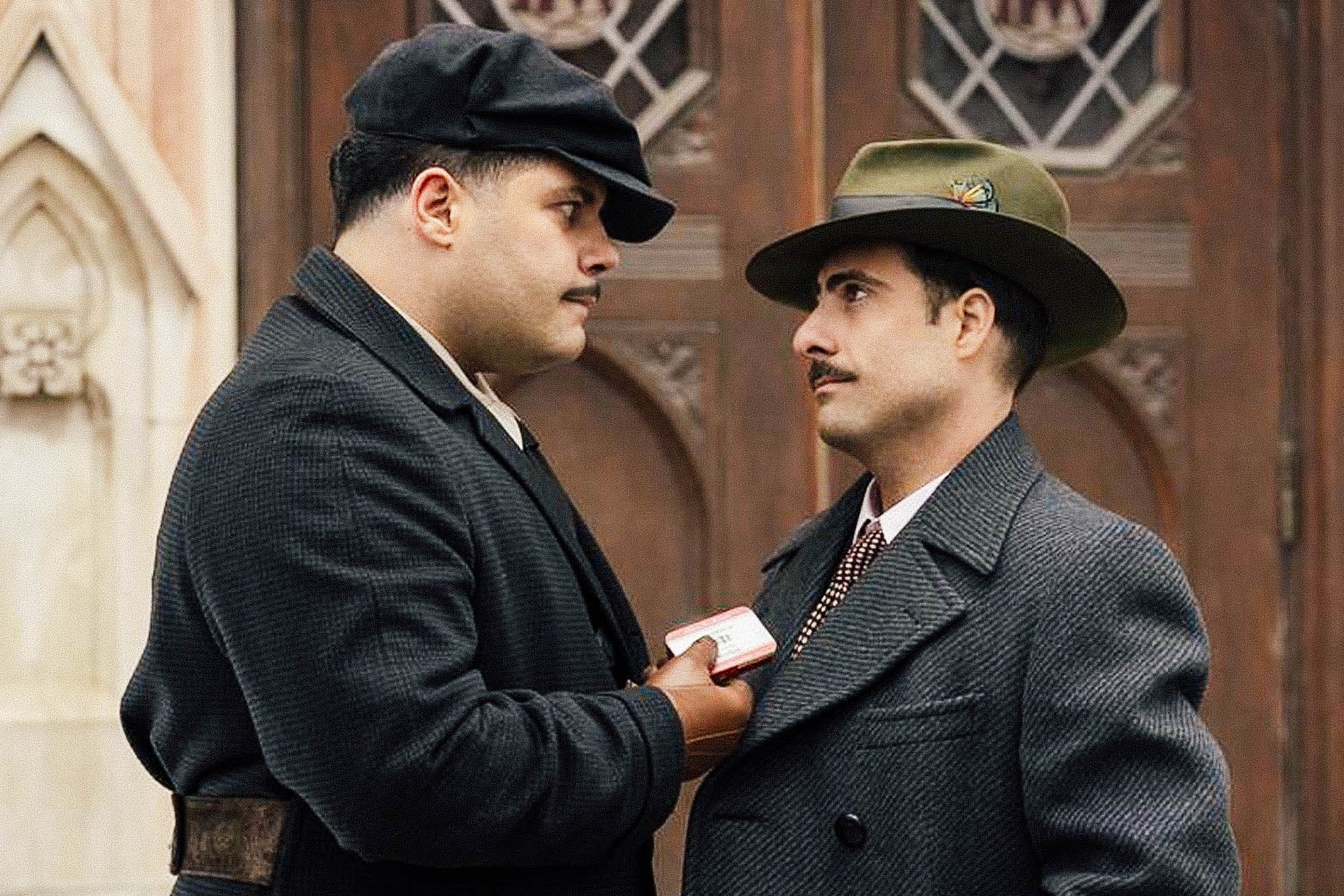 Two men with mustaches and hats stare at each other, one carrying a small tin, in a still from Fargo.