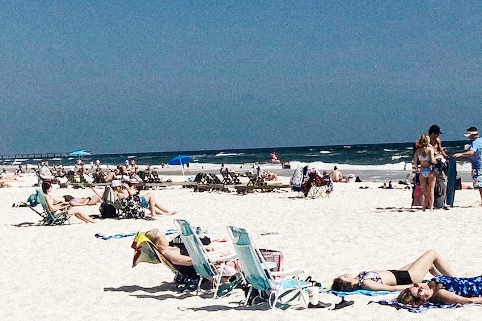 People lounging on beach chairs and towels on a sunny day at the beach