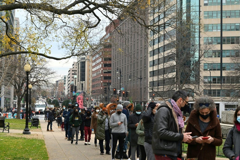 A long line of people standing on the sidewalk in a public park downtown