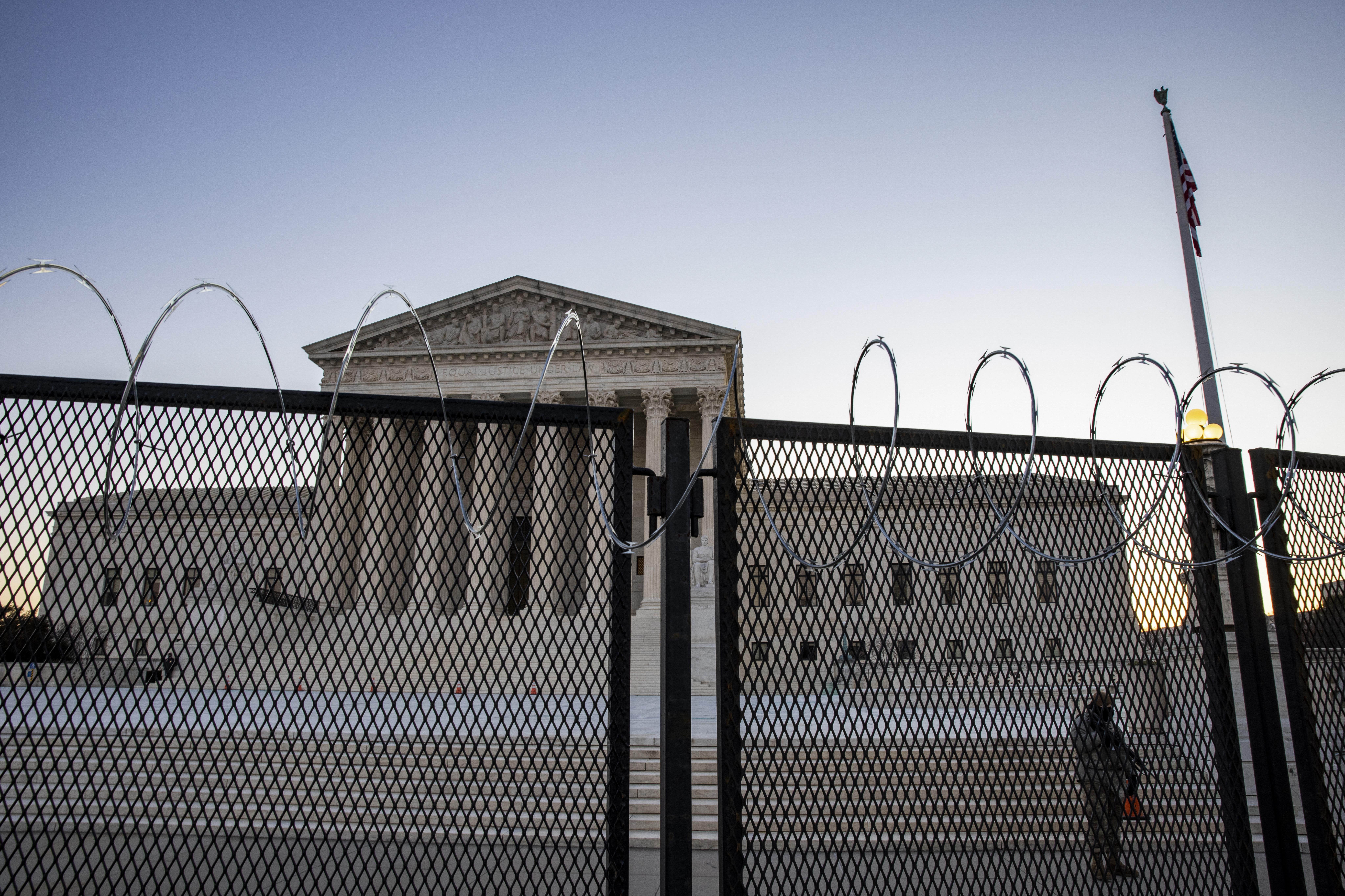 The Supreme Court is seen behind a fence. An armed guard stands in front of its steps.