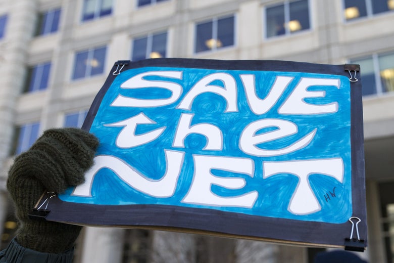 A gloved hand holds a "Save the Net" protest sign. A building is in the background.