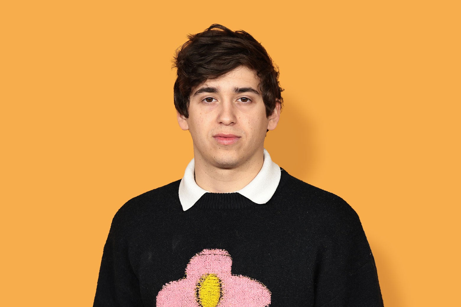 Marcello Hernández wearing a flower sweater, against an orange background.