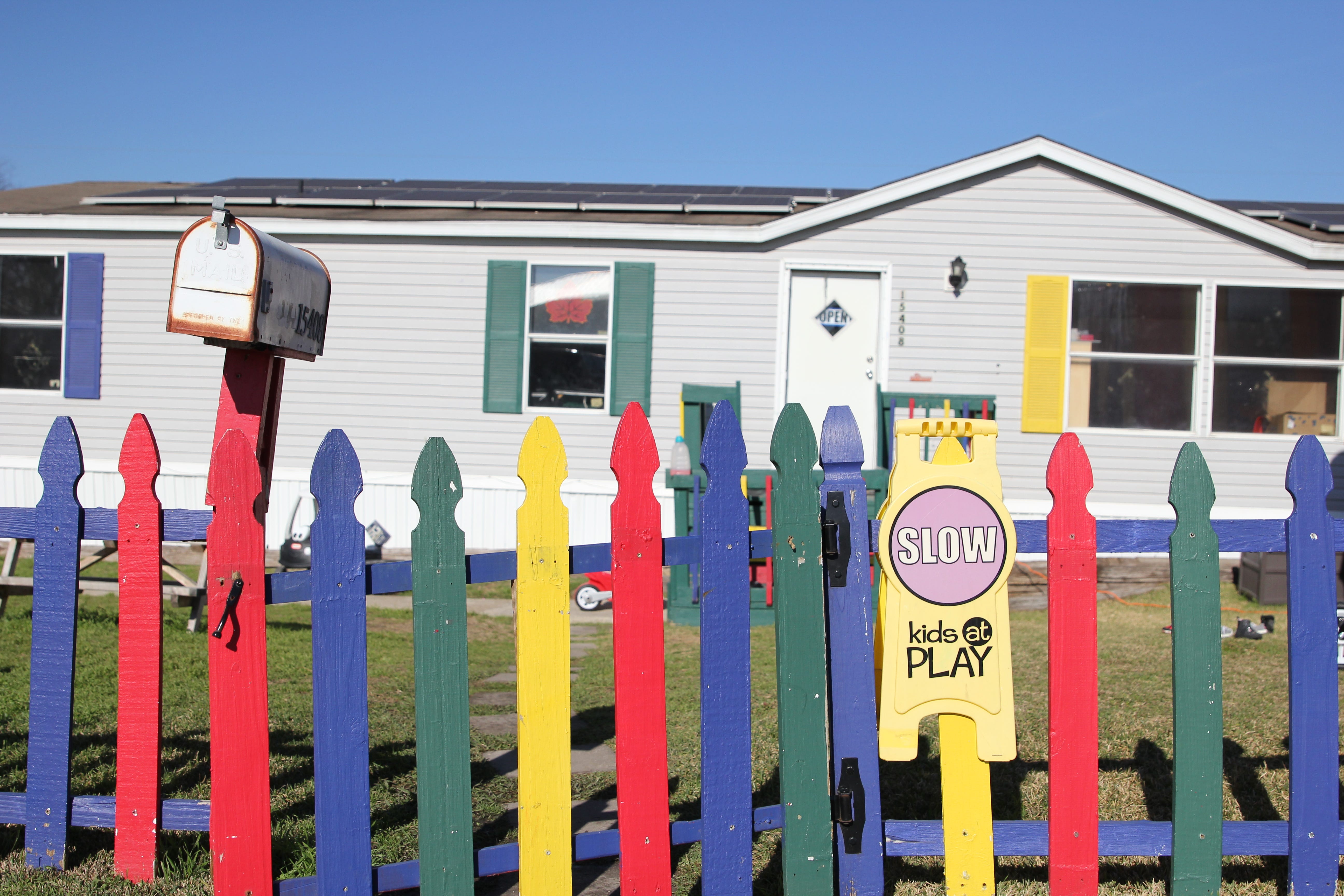A sign reading "Slow. Kids at Play" is seen hanging on a multicolored fence in front of a suburban house.