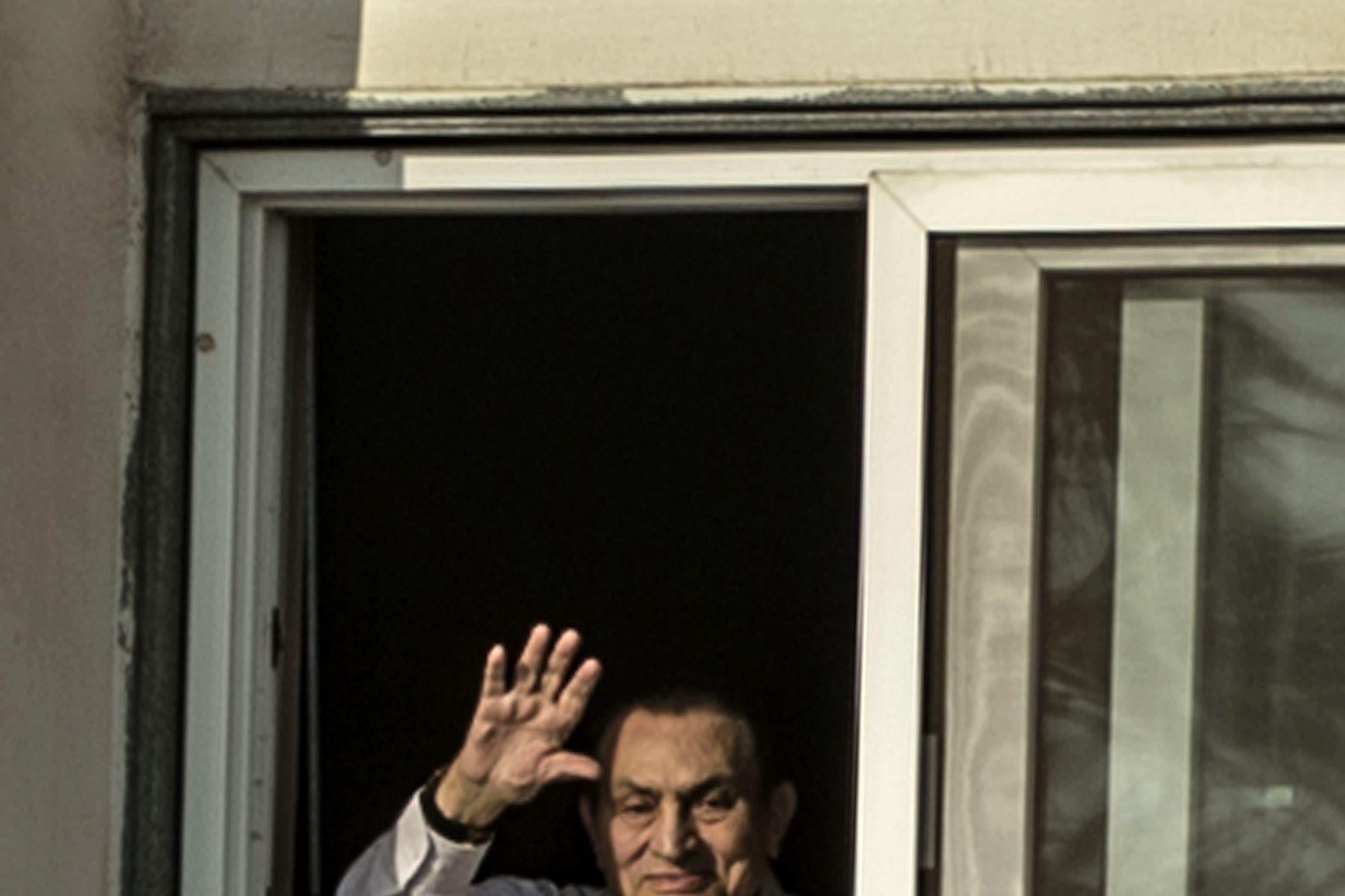Egypt's former president Hosni Mubarak waves out a window over a railing.