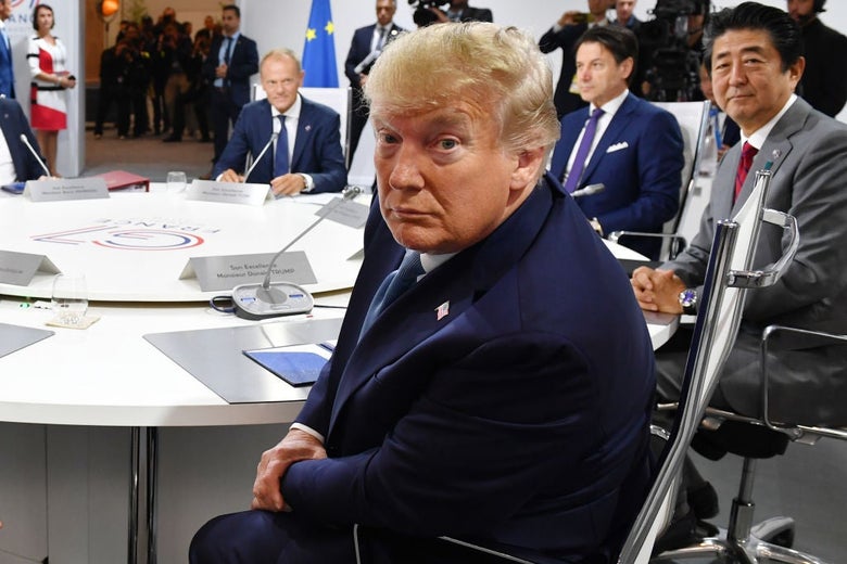 Trump, seated at a conference table with other world leaders, turns in his chair to look toward the camera.