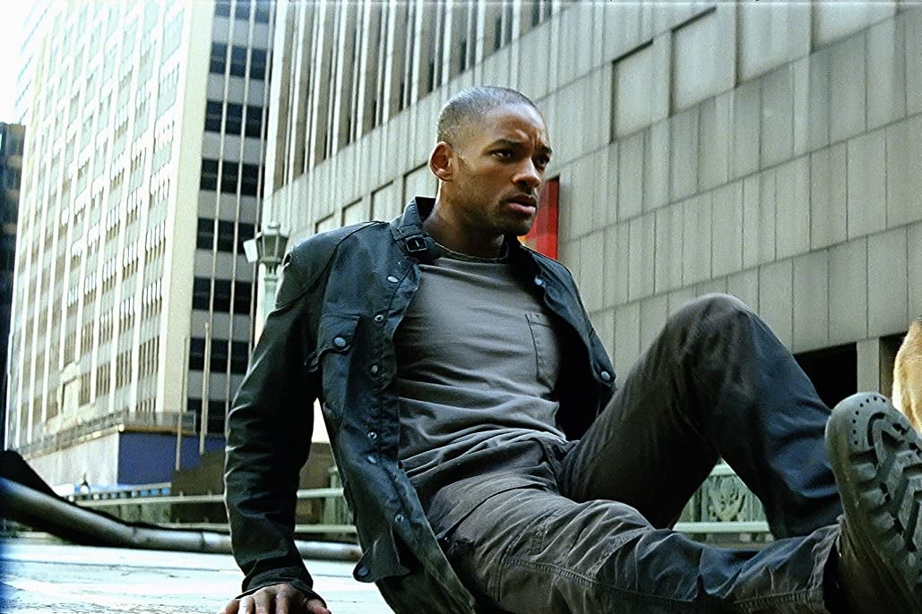 Will Smith sits on a city sidewalk, brow furrowed. A dog's rear end is in frame.