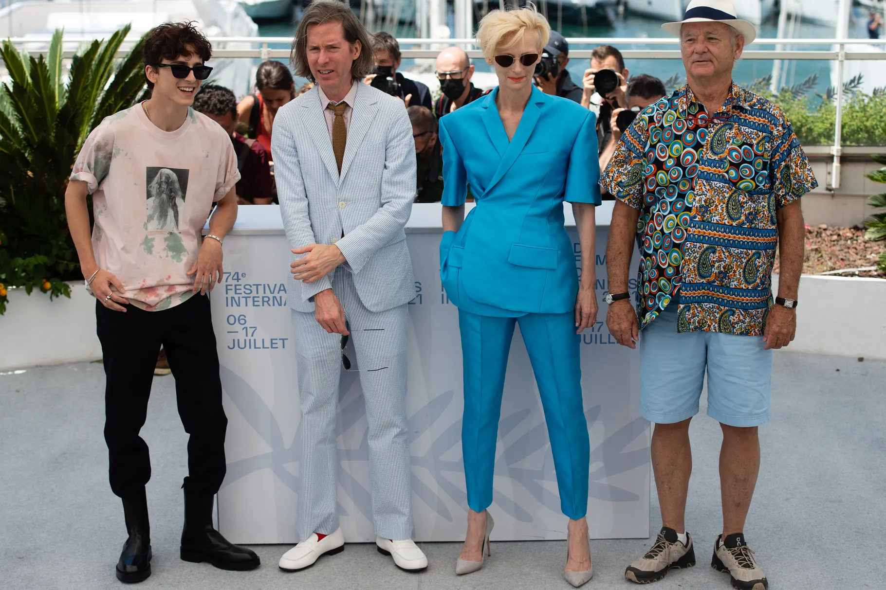 Four people stand in a row: two men, then one woman, then another man. 