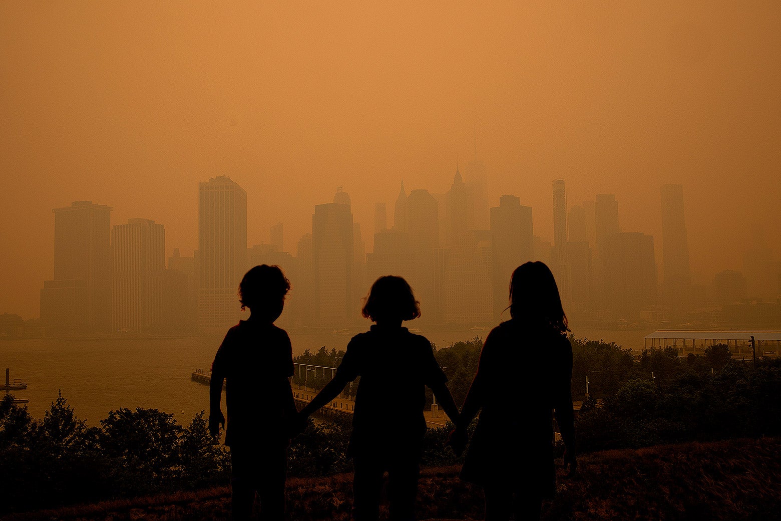 Three children holding hands while looking at the orange haze of New York City as smoke blankets the city.