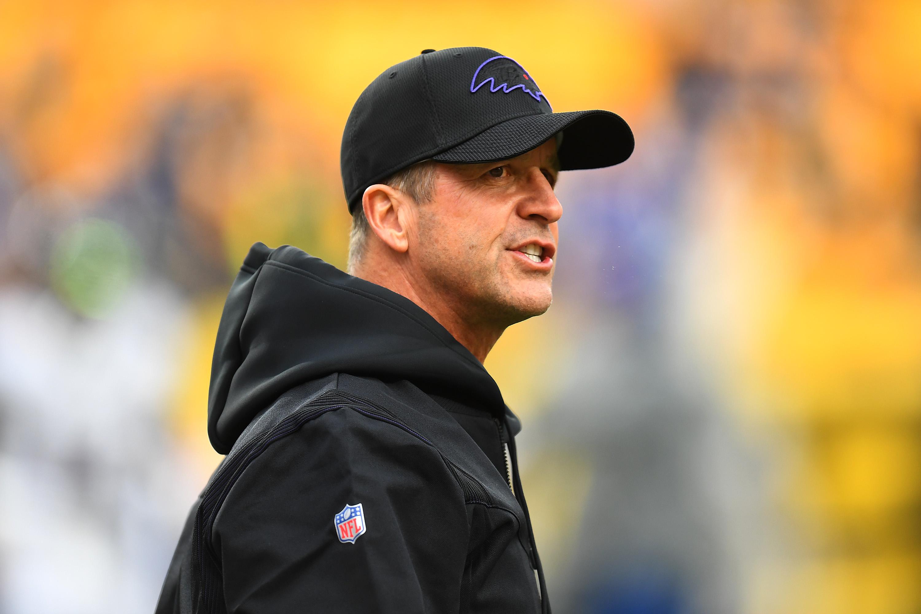 Harbaugh speaking with a hooded jacket and Ravens hat on, on the sideline