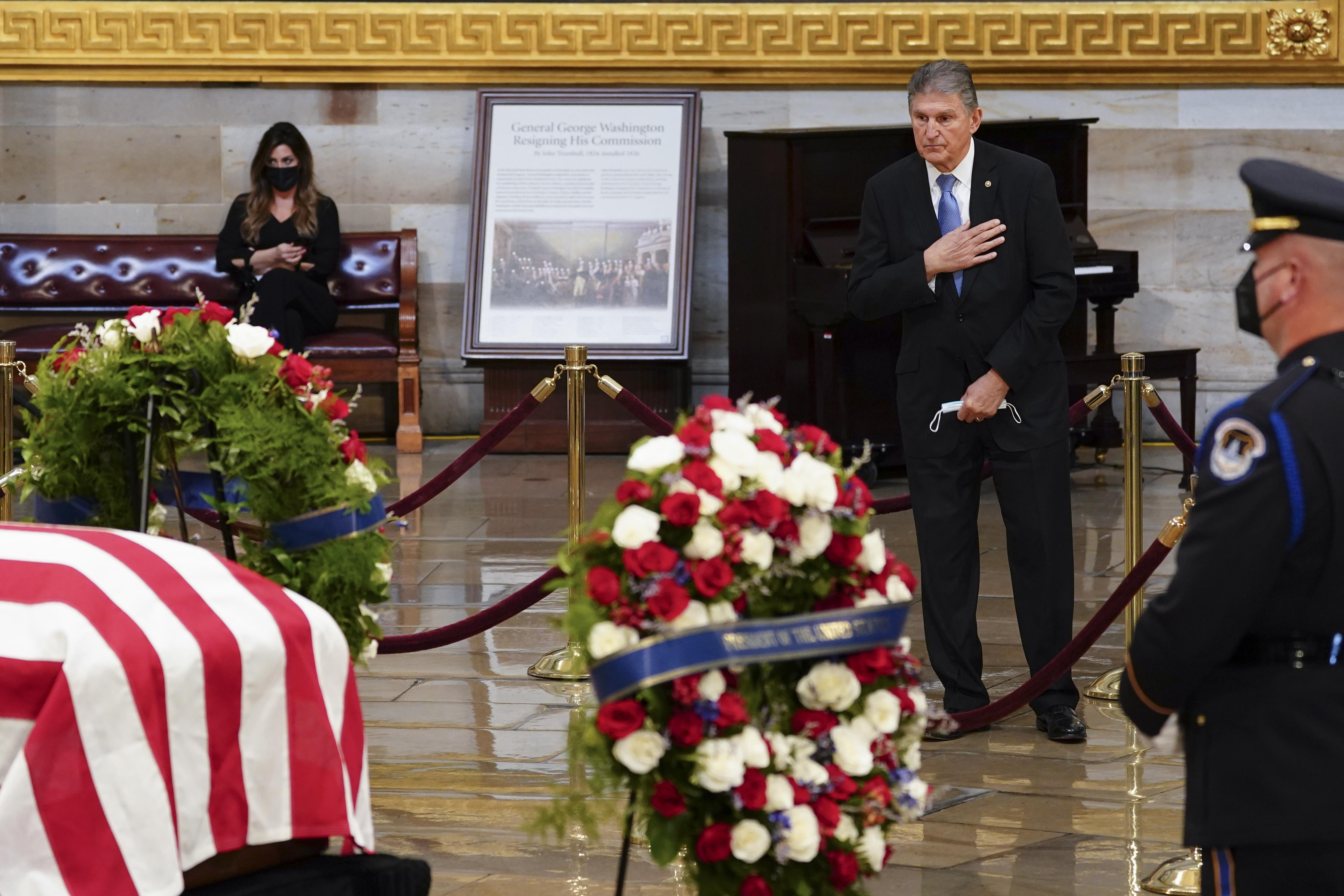 Joe Biden stands with his hand on his heart in the midst of a state funeral procession.