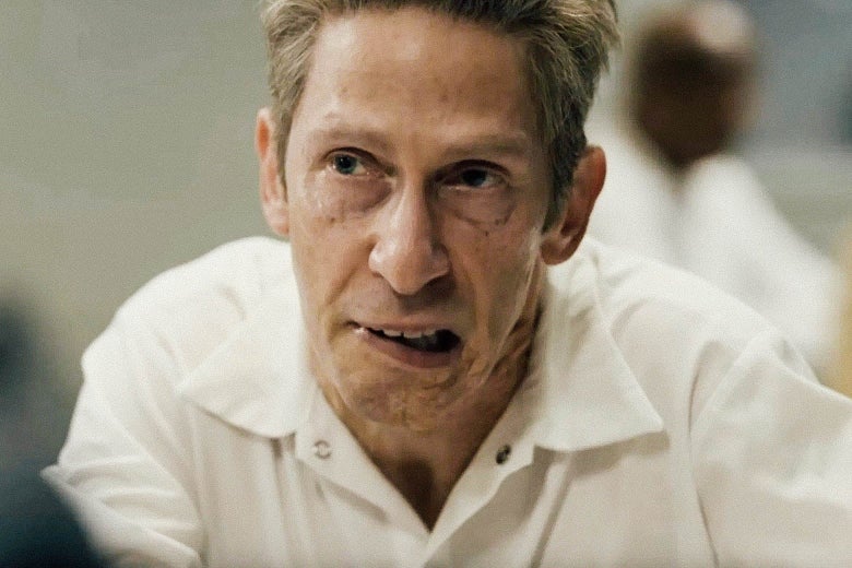 Tim Blake Nelson in a prison uniform, his mouth twisted to one side