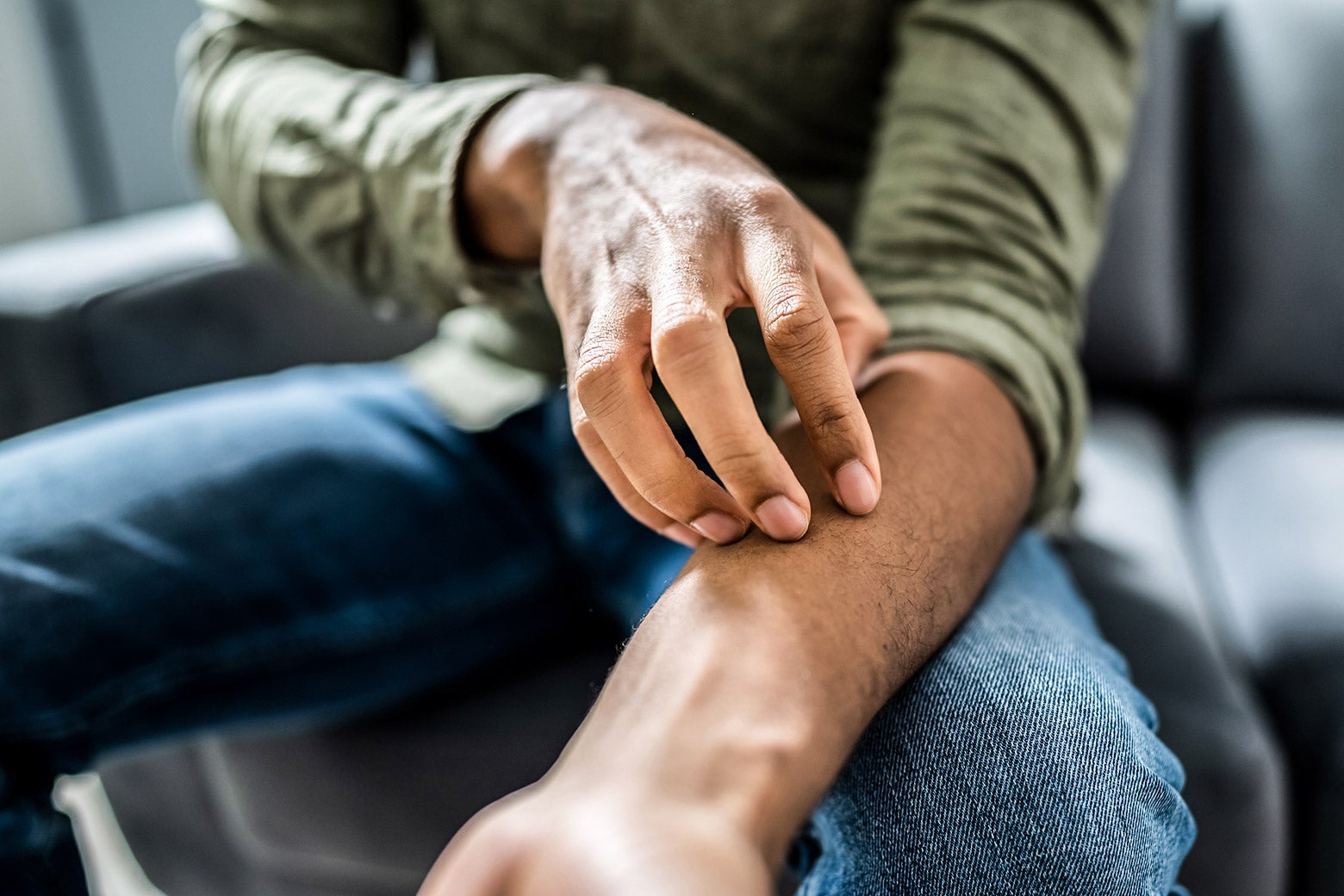 A person with rolled-up sleeves scratches their left forearm.