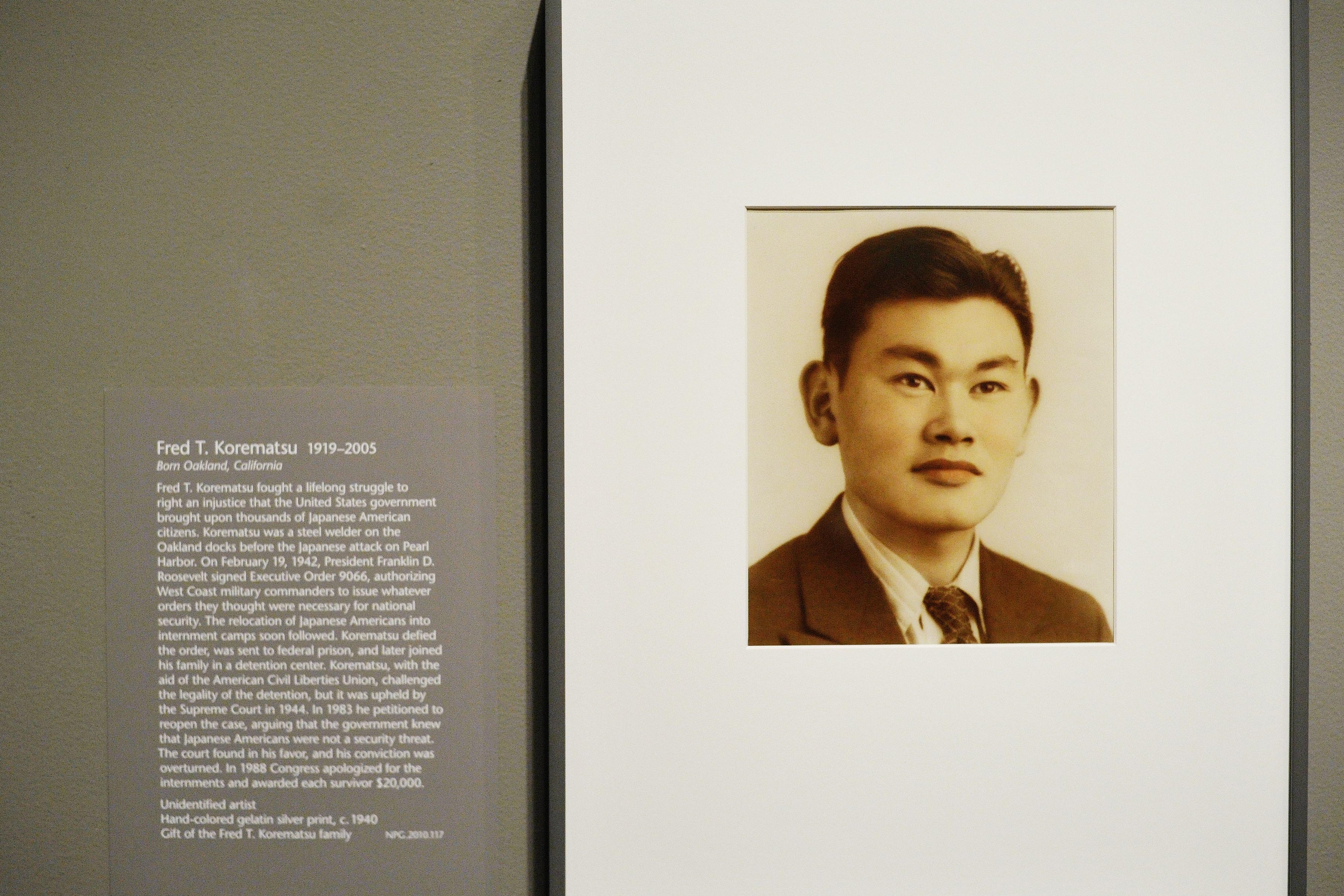 A framed sepia-toned portrait of Fred Korematsu on a gray wall with explanatory text next to it.