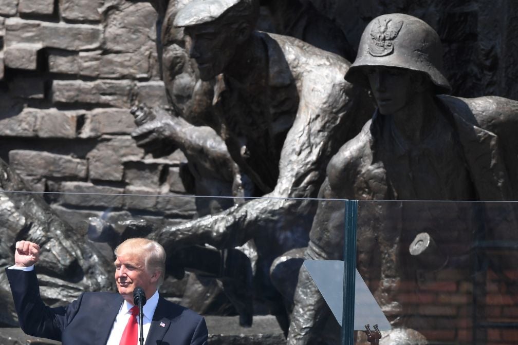 Trump raises his fist in front of a large statue of a soldier.