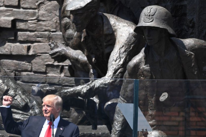 Trump raises his fist in front of a large statue of a soldier.
