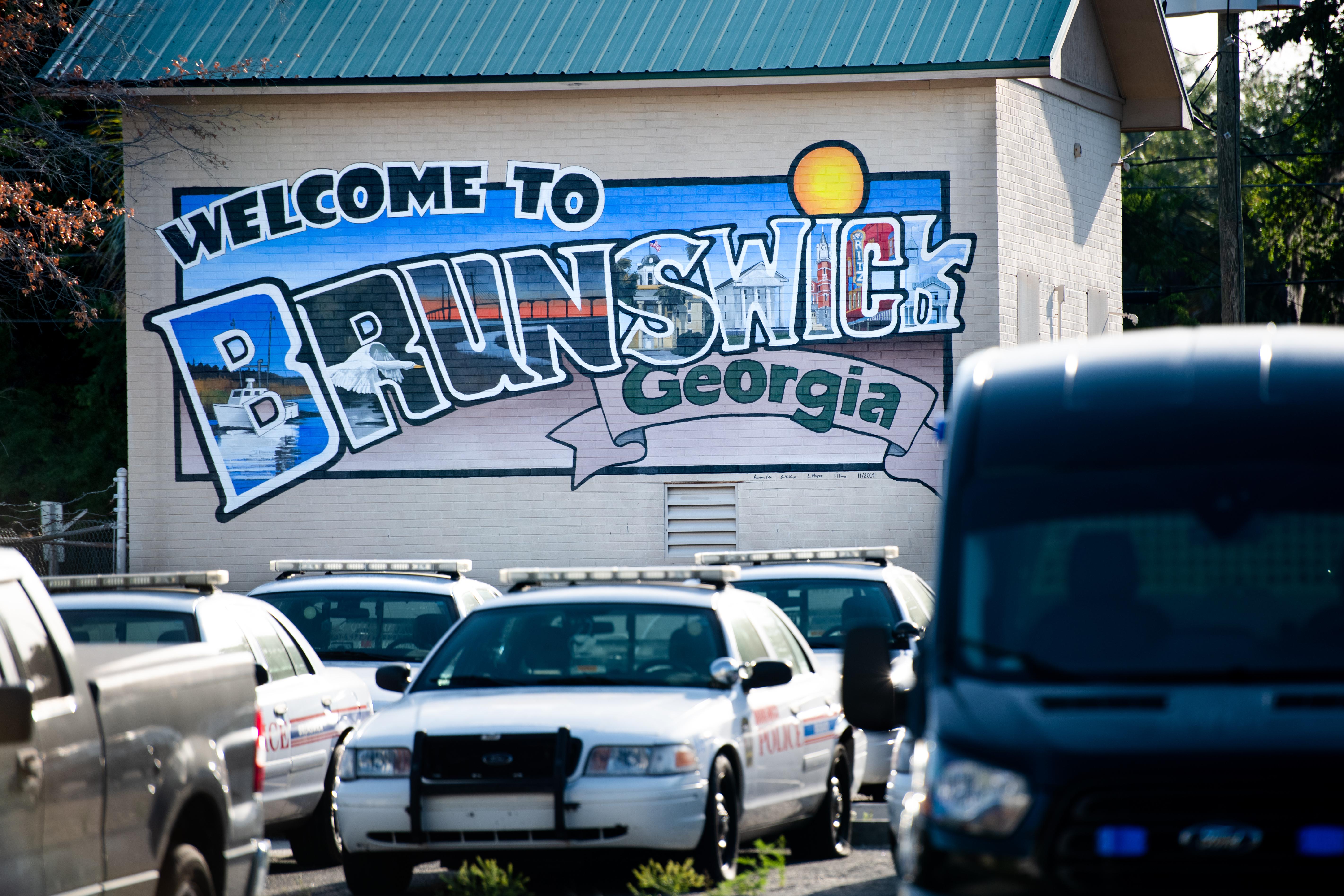 A mural that says "Welcome to Brunswick Georgia" on a building with police cars parked in front of it