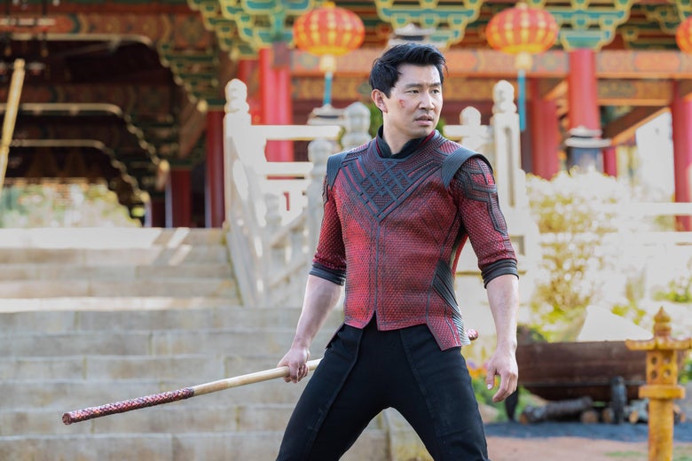 Simu Liu in a tight red shirt and carrying a big stick in Shang-Chi and the Legend of the Ten Rings