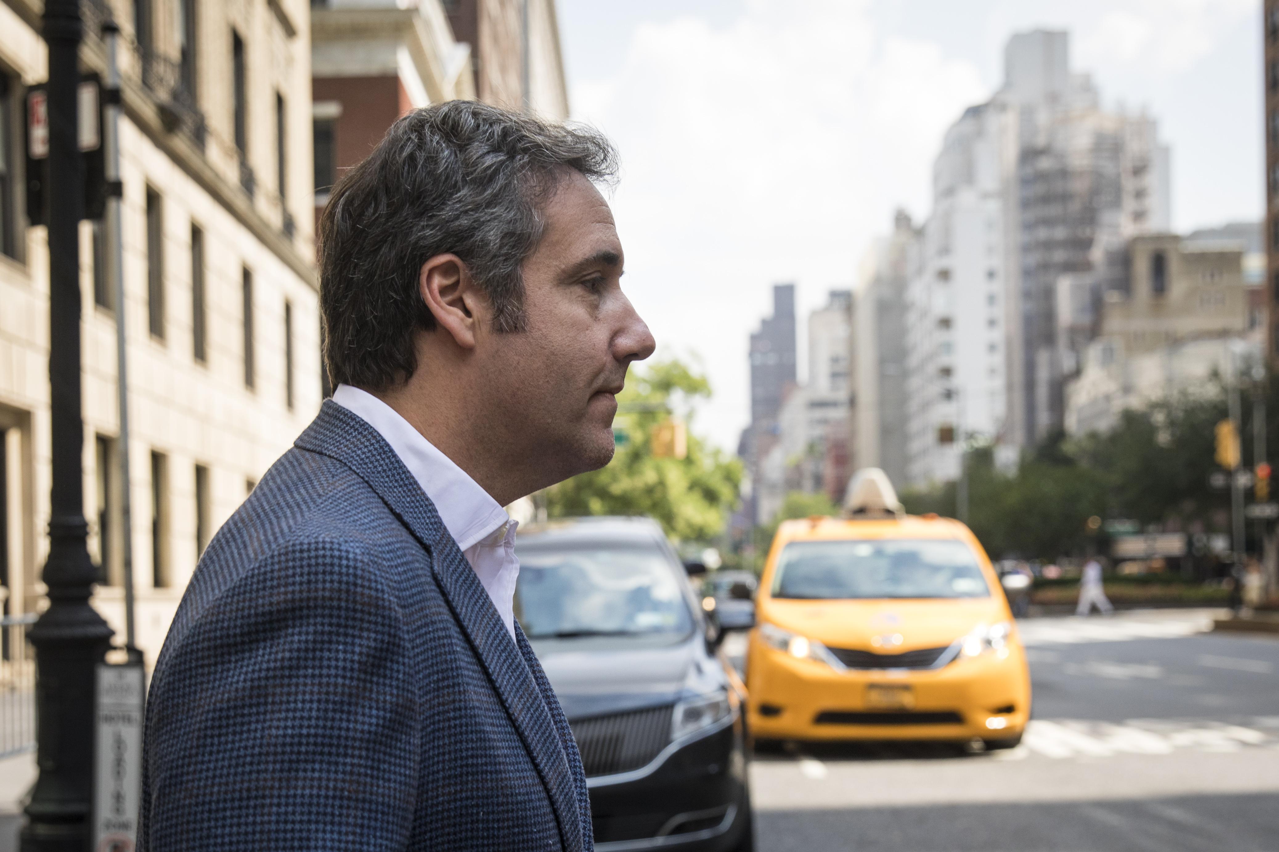 Michael Cohen walks on a New York City street in front of a yellow taxi cab.