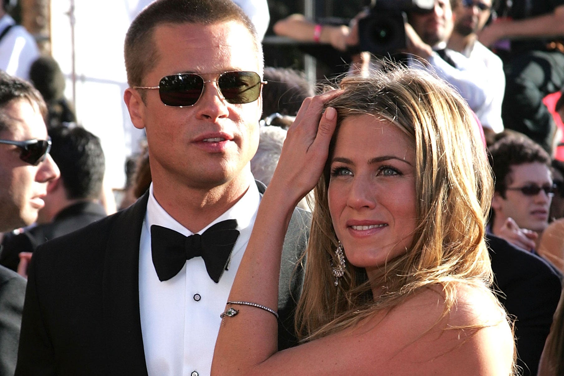 Brad Pitt in a tuxedo and aviator sunglasses stands next to a smiling Jennifer Aniston.