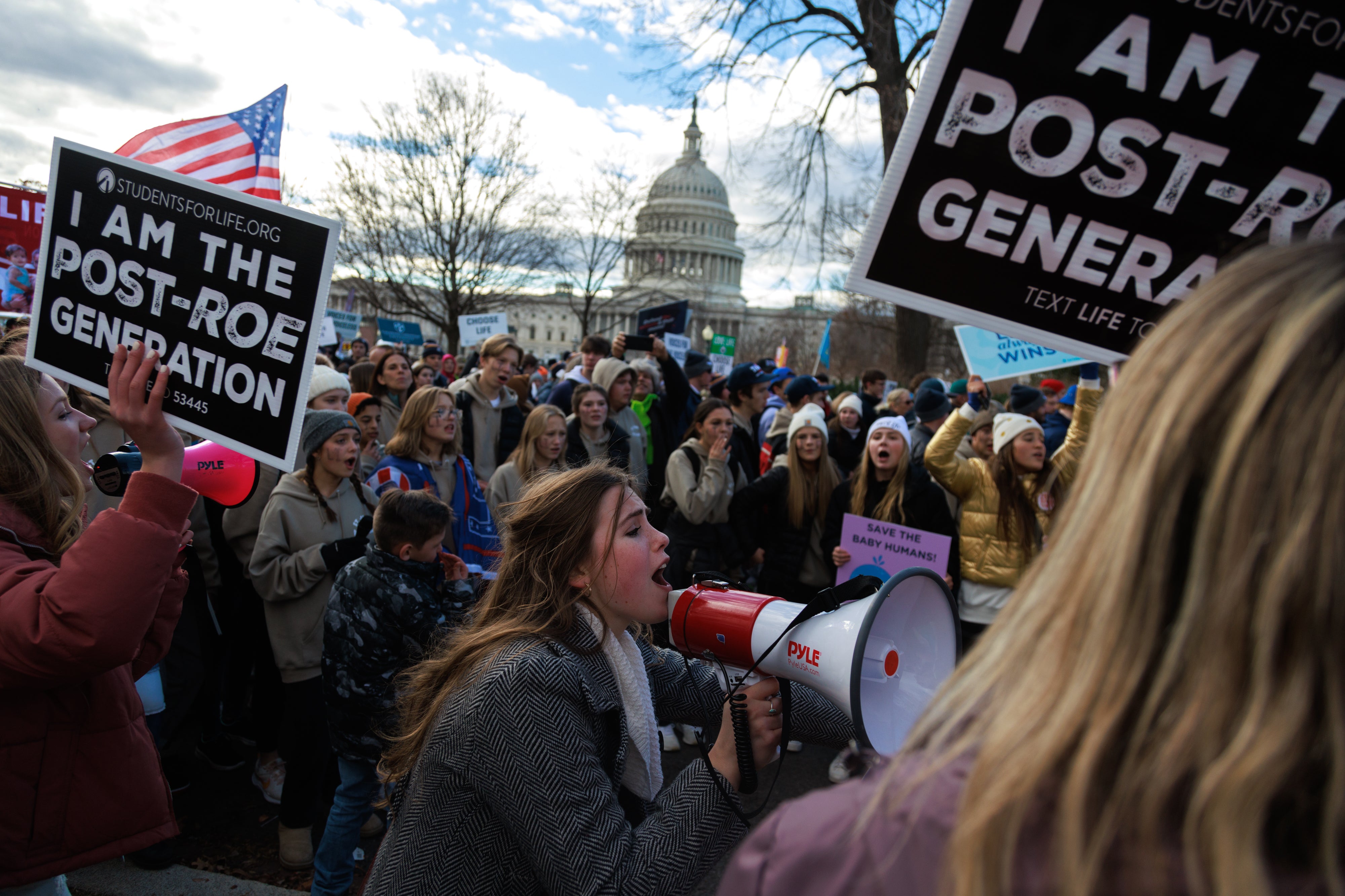 A woman shouts into a megaphone amidst a crowd of protesters carrying anti-abortion signs in front of the U.S. Capitol.