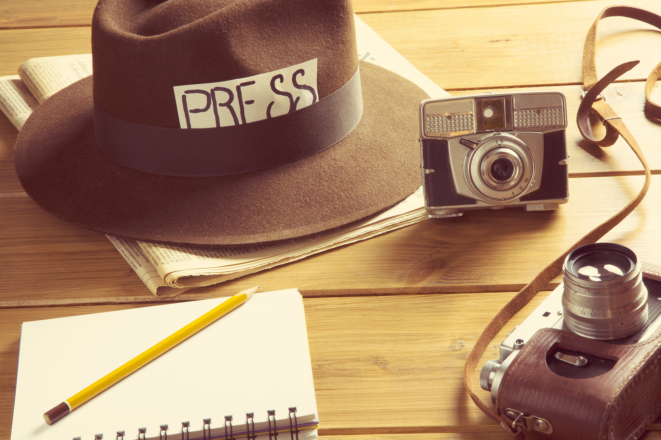 Journalism tools on a table, including a camera, notebook, and press hat.