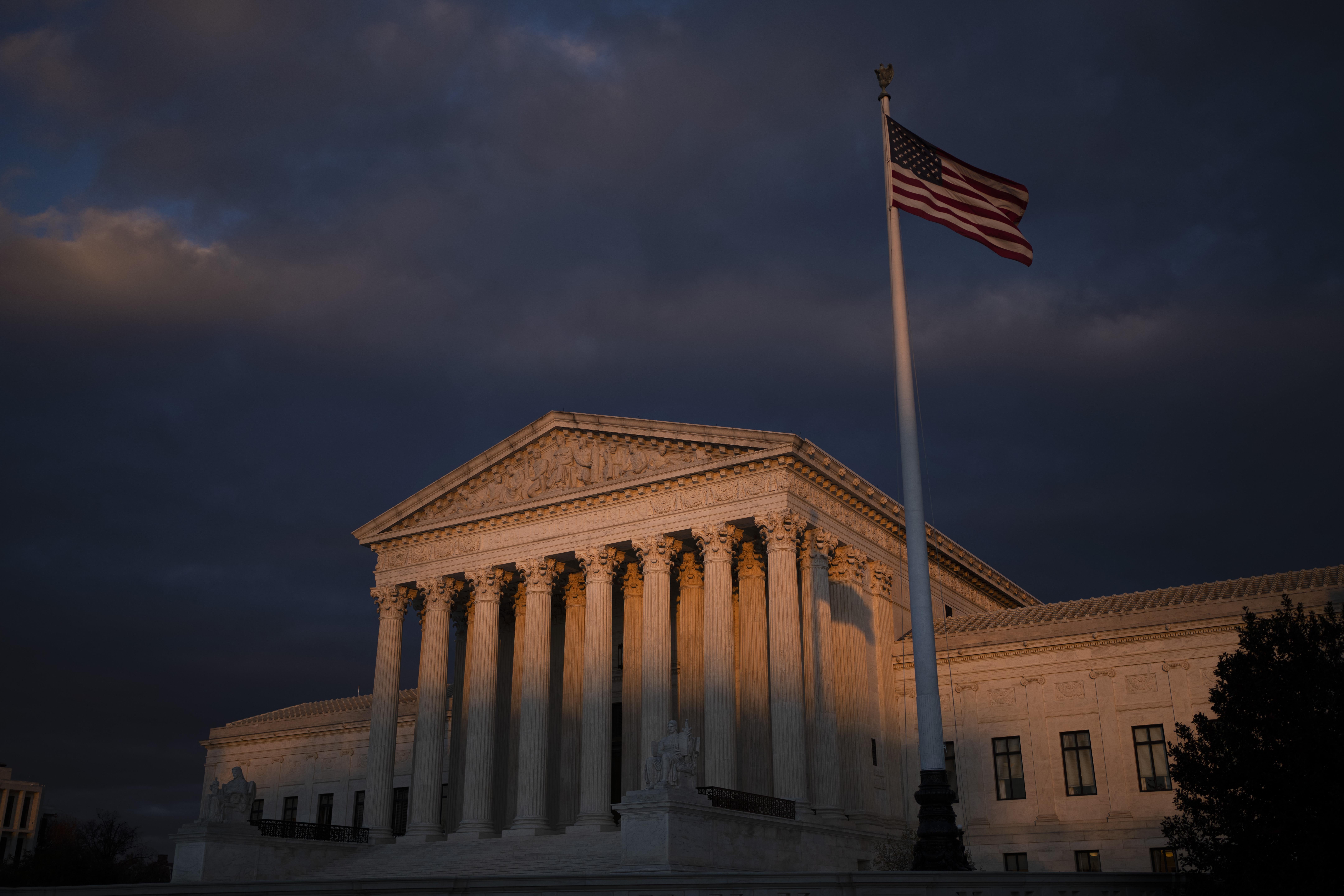 Night falls on the Supreme Court as an American flag flaps in the wind.