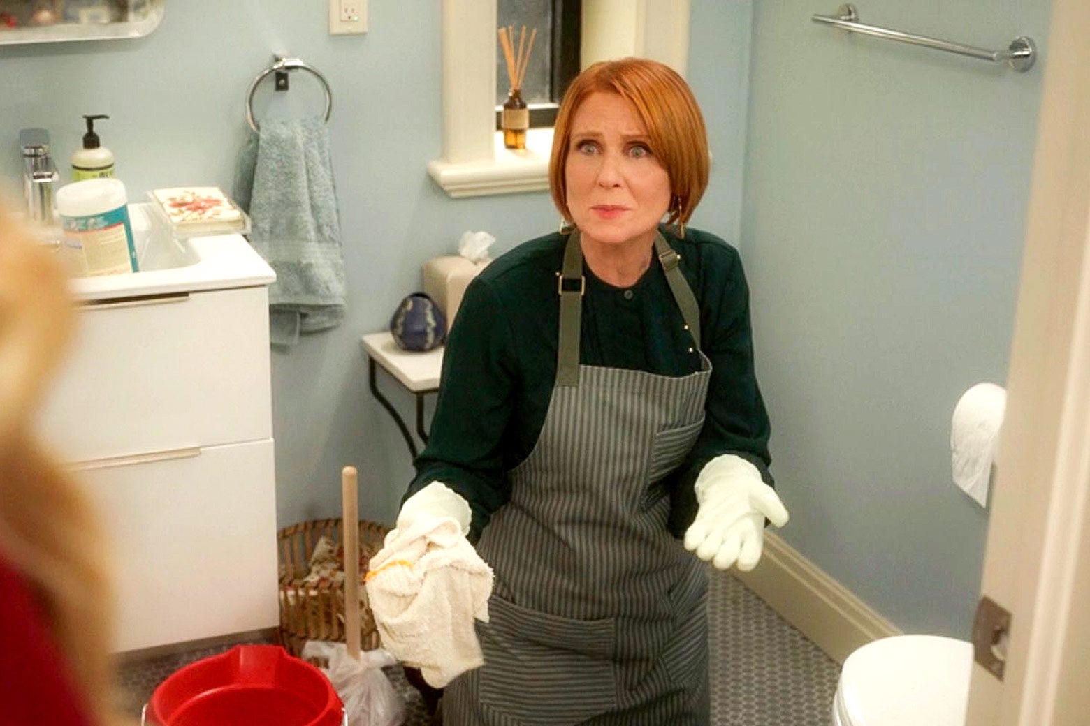 Miranda está arrodillada en el suelo del baño mirando hacia arriba y parece molesta.