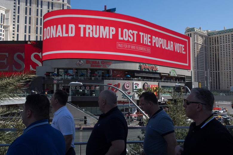 People walk by a second billboard paid for Mike Bloomberg, saying Trump lost the popular vote.