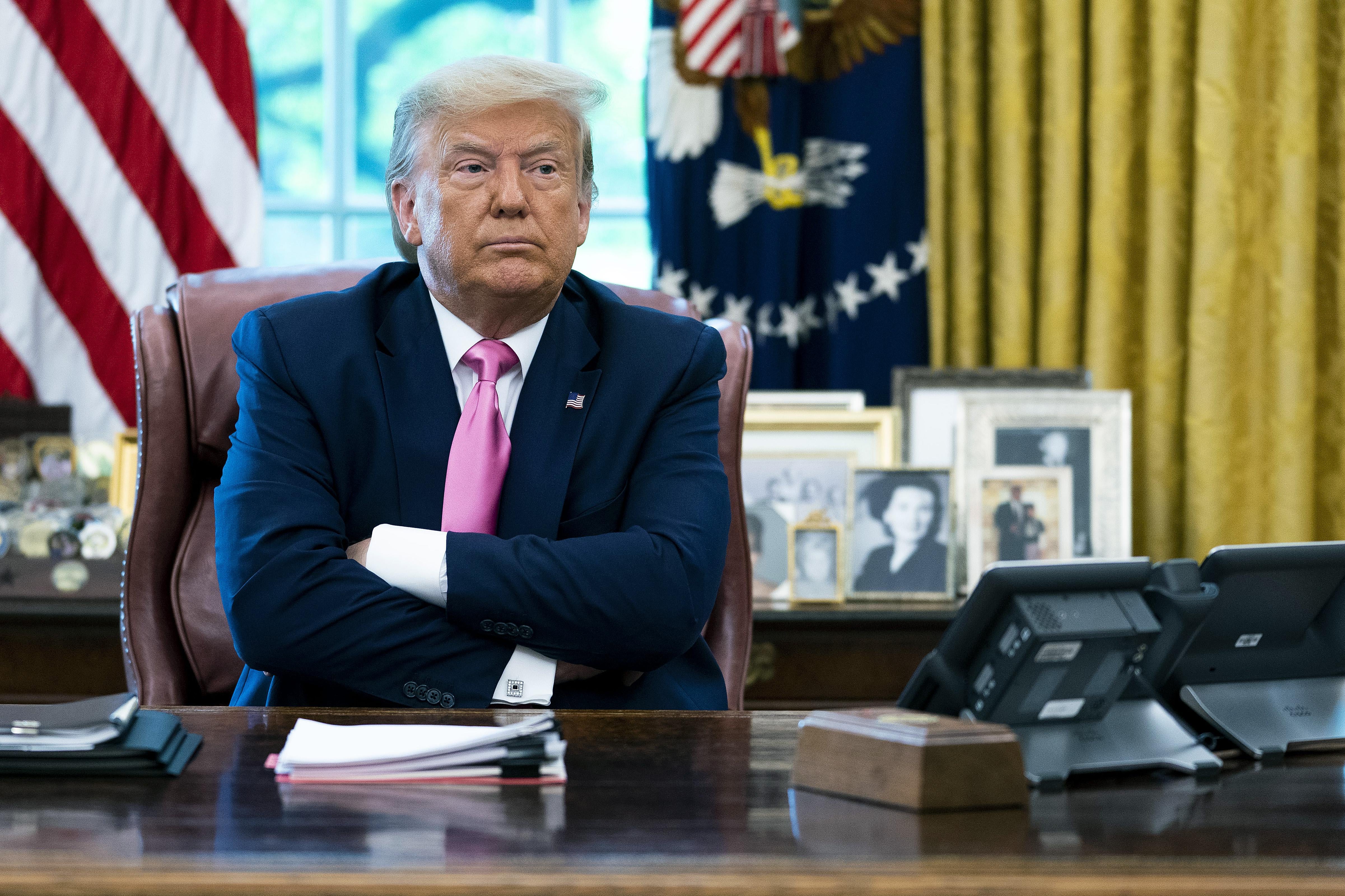Trump sits with his arms crossed at the Resolute Desk