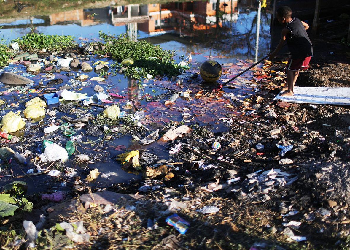 A boy reaches for a ball along a polluted canal in the Mare favela community complex on July 18, 2016 in Rio de Janeiro, Brazil. 