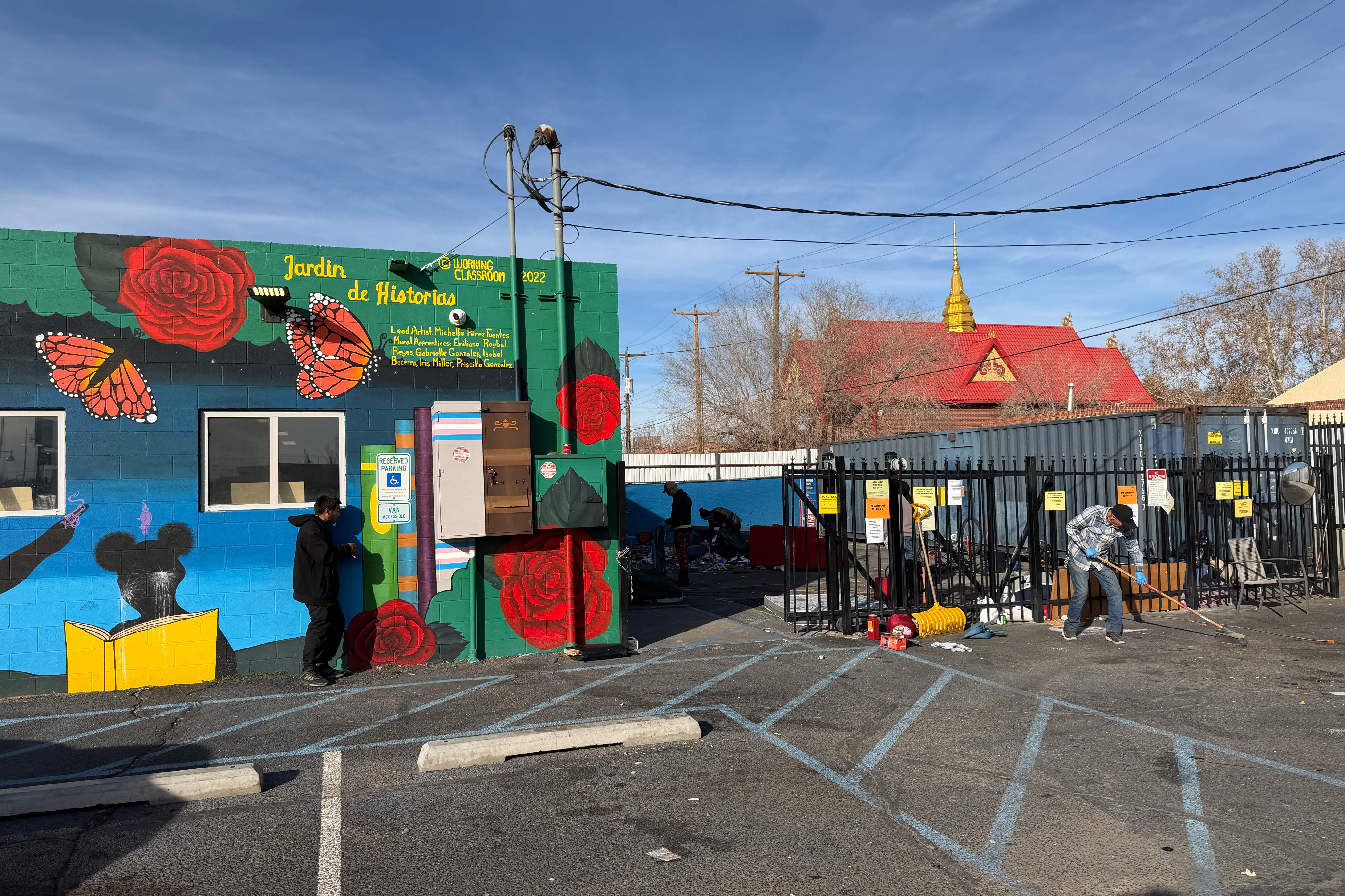 A man sweeping the parking lot near a building with a colorful mural.