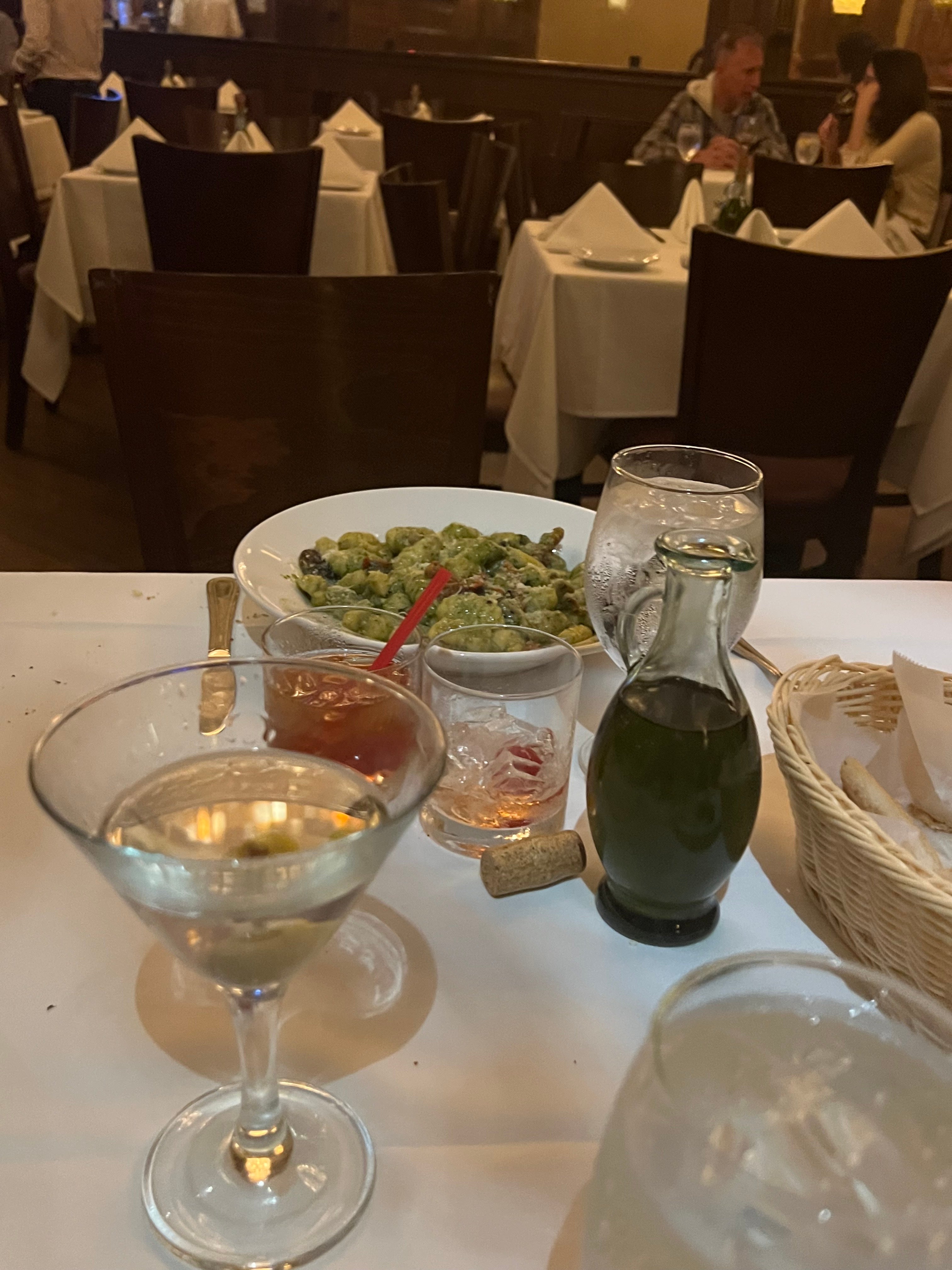 A photo of pasta and martini on a white table cloth.